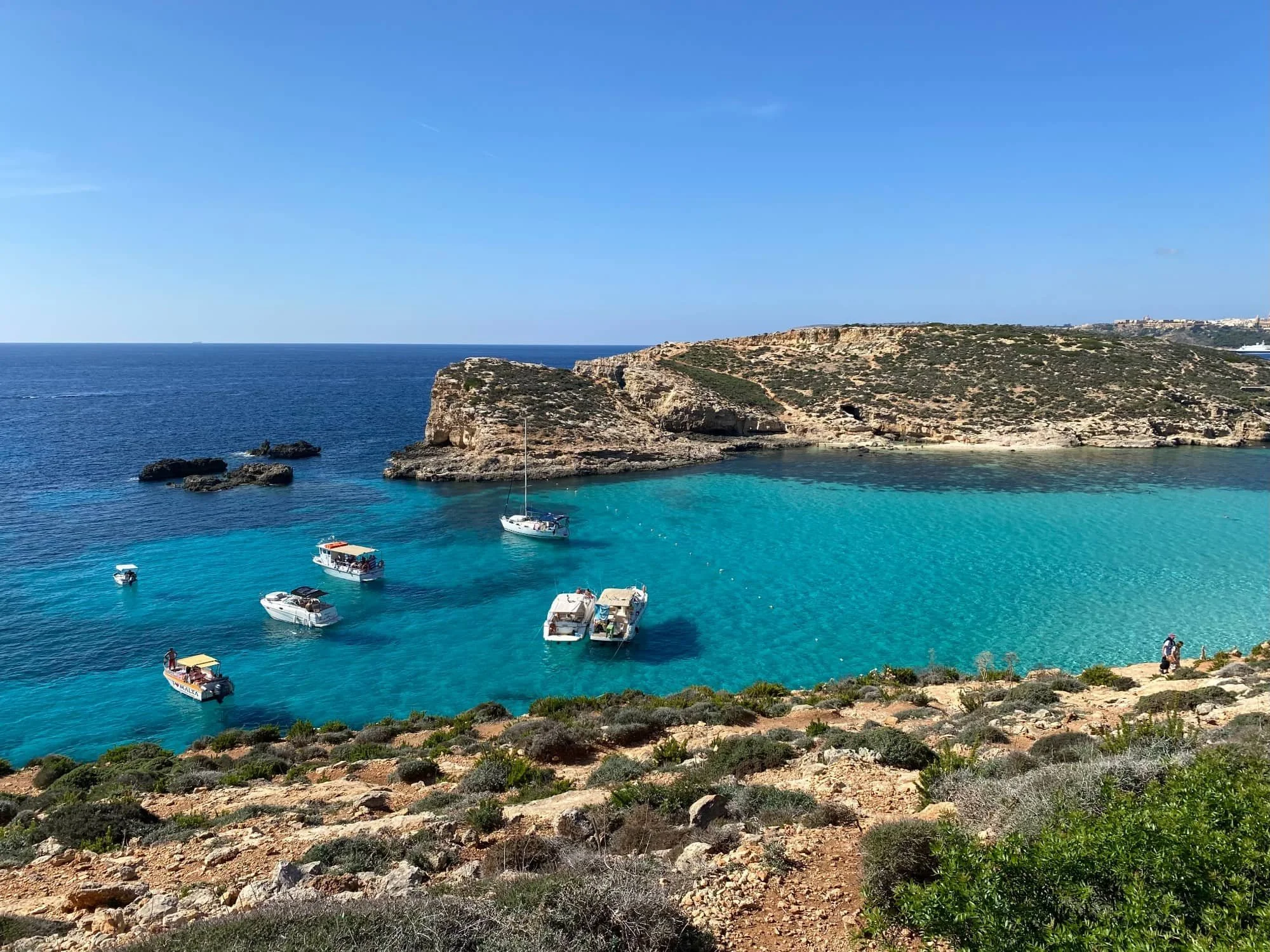 A stunning view from the cliffs overlooking the bright blue water and rocky coastline of the Blue Lagoon.