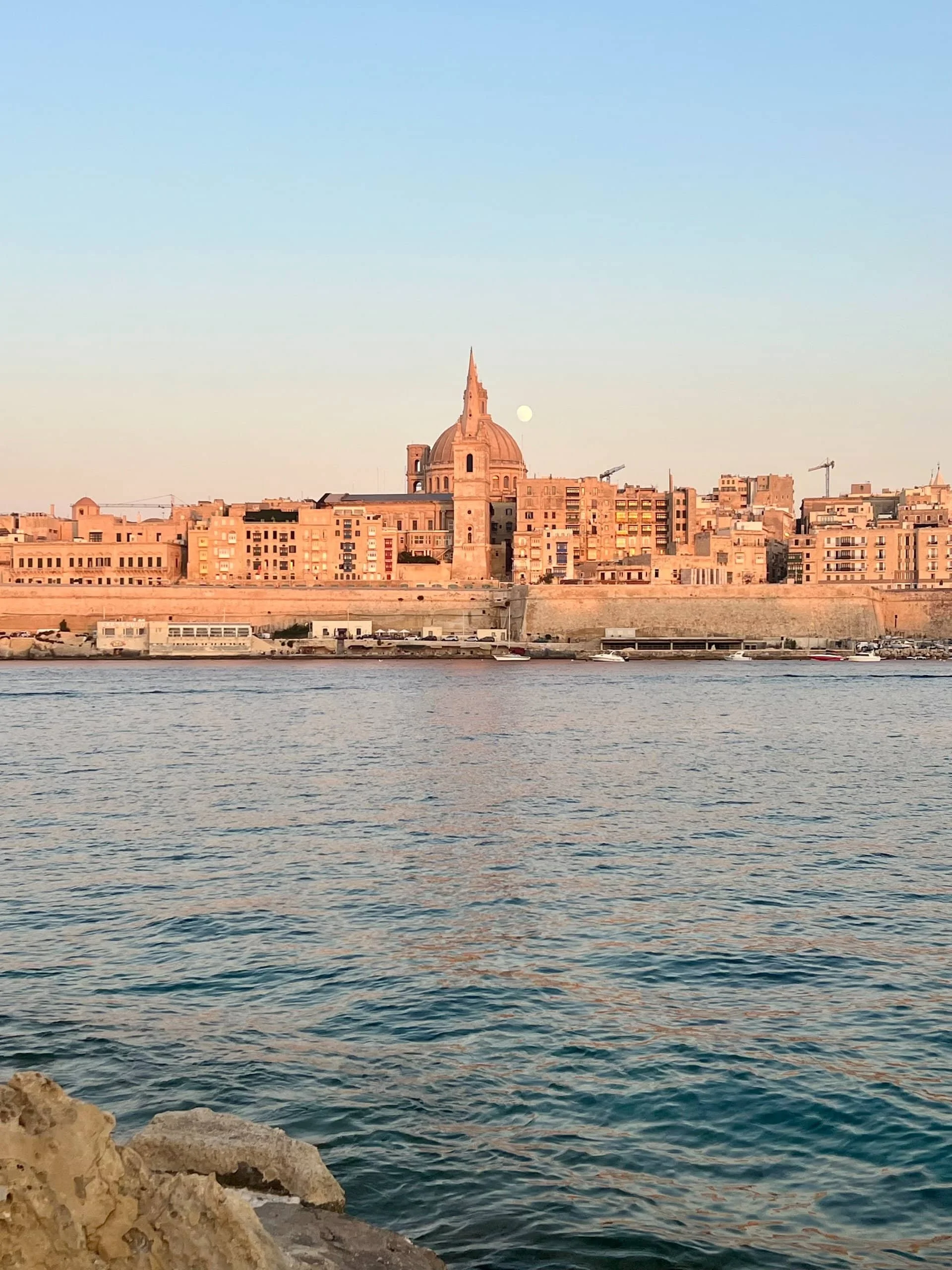 A stunning view of the Basilica of Our Lady of Mount Carmel and Valletta skyline seen from Stone Beach at sunset.