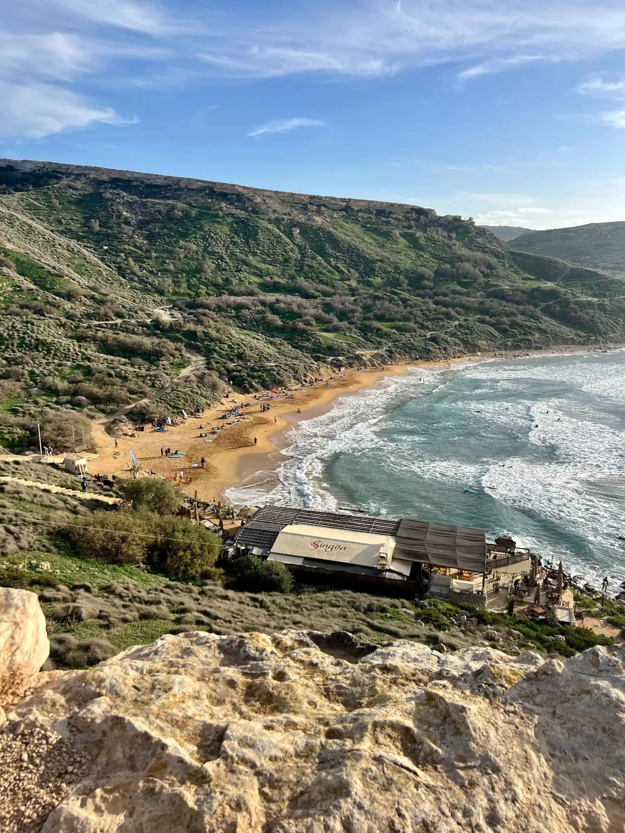 Panoramic view of the green clay slopes and waves rolling into Għajn Tuffieħa Bay.