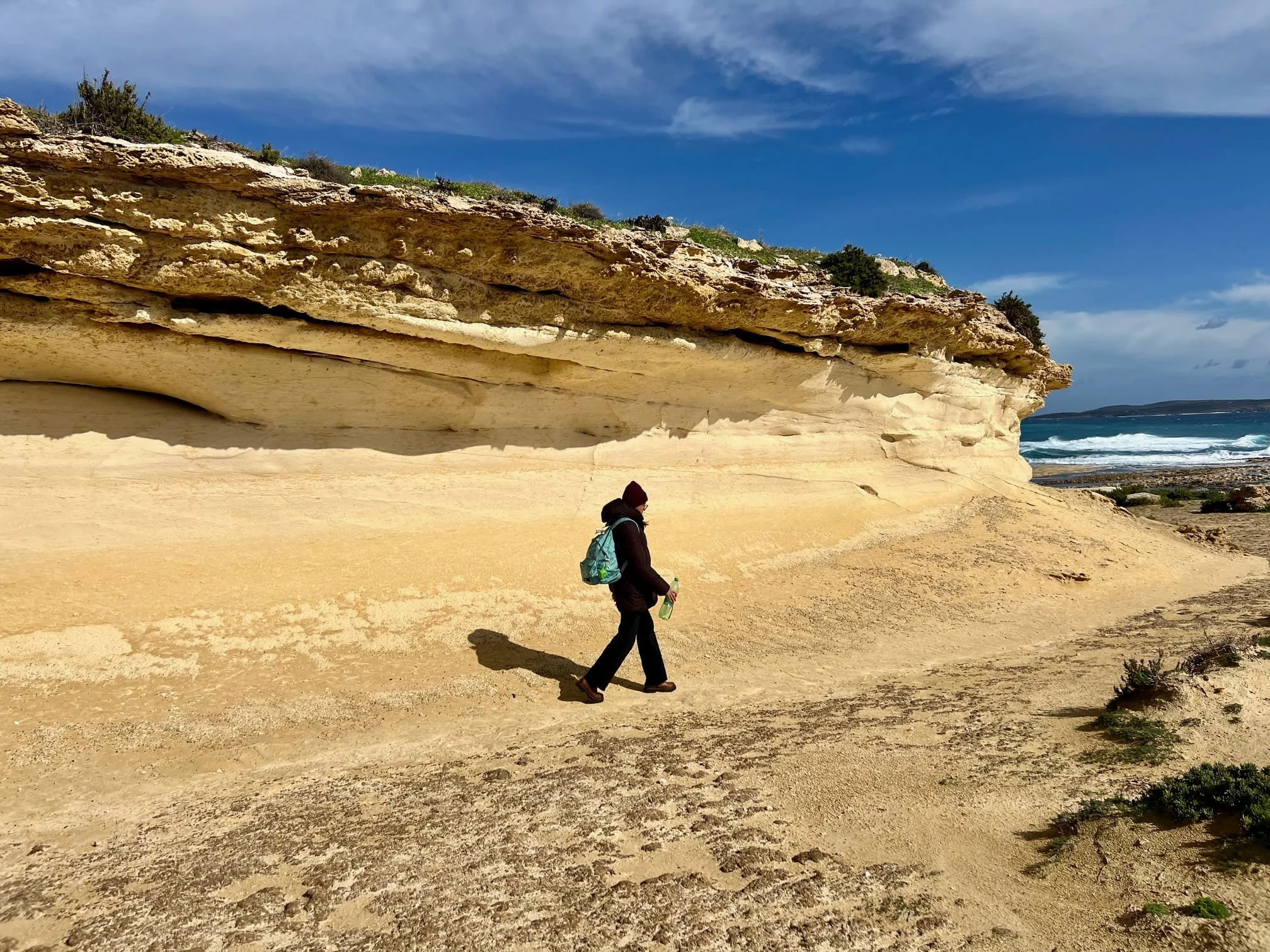 Hiker walking past massive, eroded limestone rock formations on the coastal trail between Xatt l-Aħmar and Ras il-Hobz in Gozo.