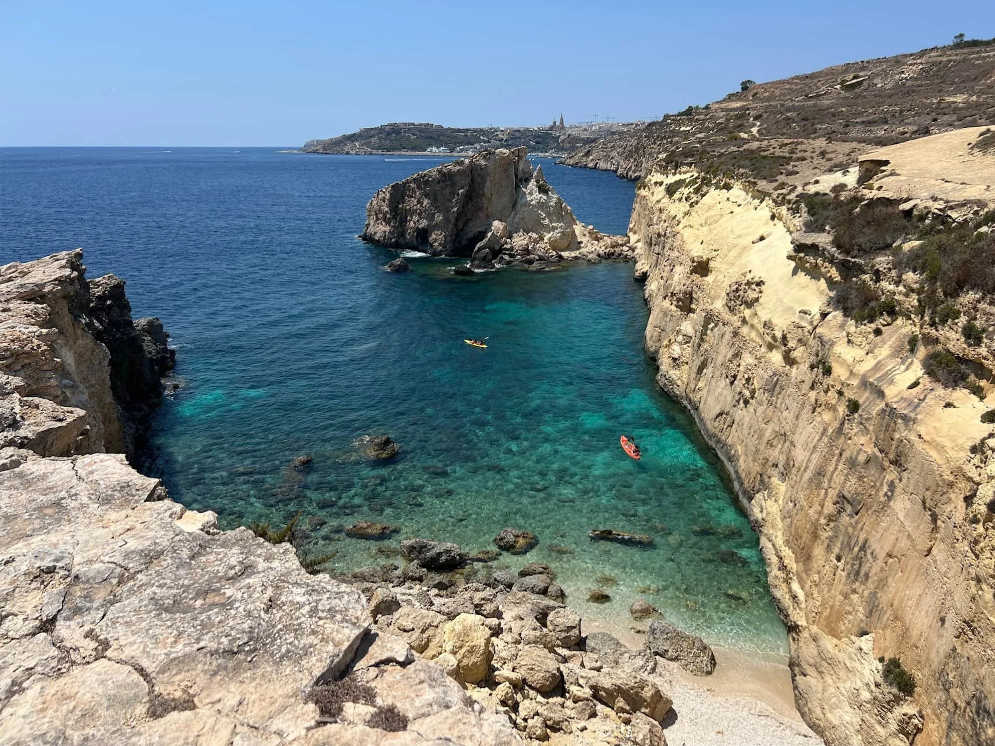 View from the Barbaggan Rocks looking towards Mgarr Harbour with clear blue water.