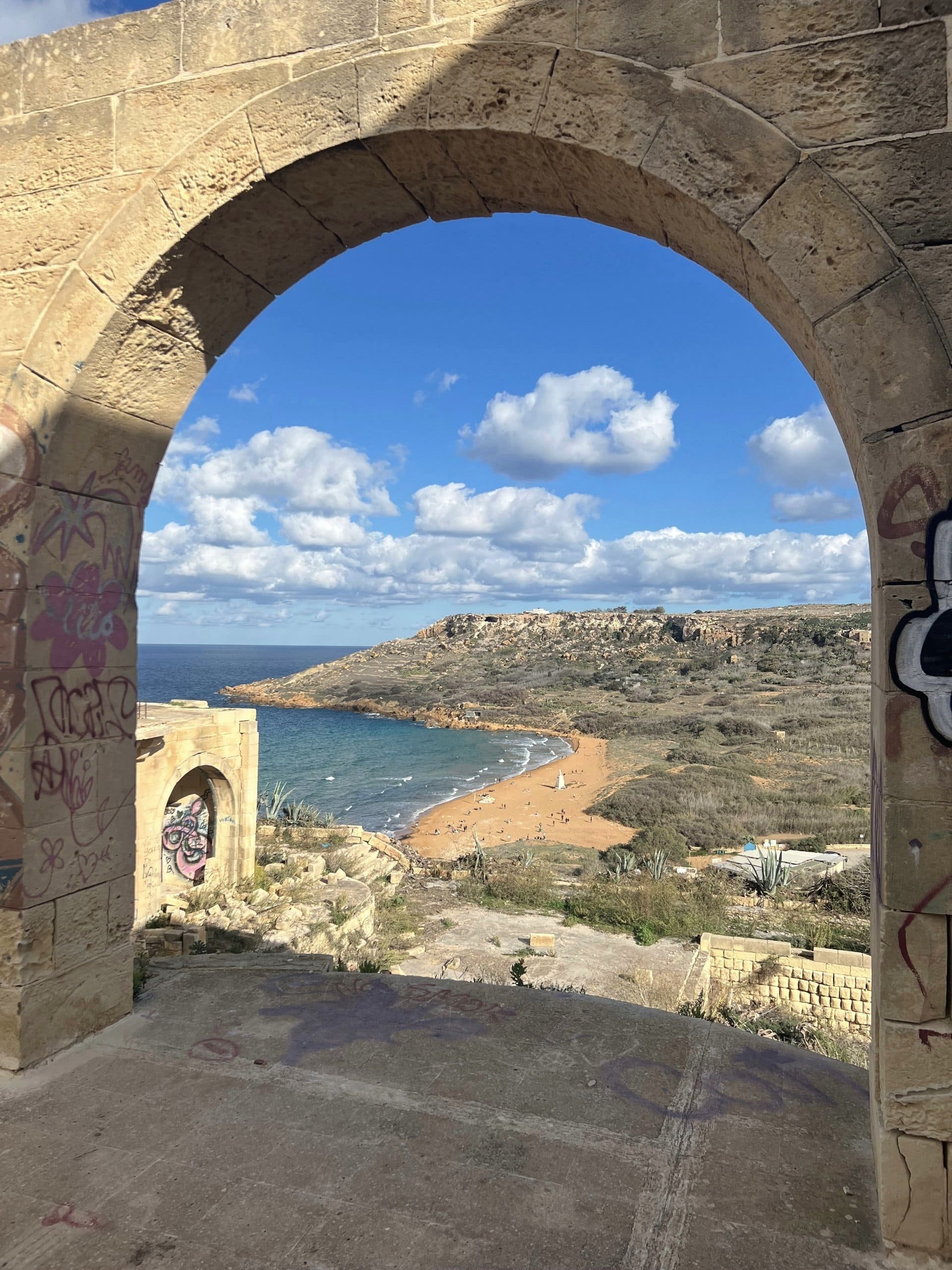 A stunning view of the red sands of Ramla Bay framed through the stone arch of Tal-Mixta Cave.