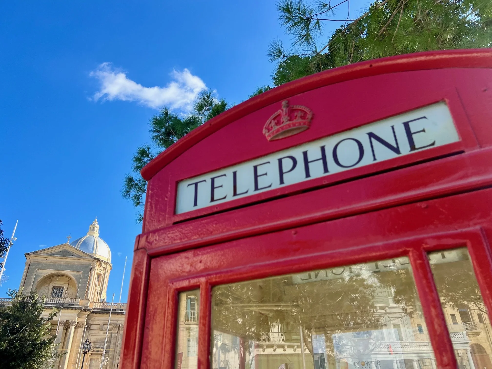 A classic red British telephone booth standing in Archbishop Gonzi Square with the St. Joseph Parish Church in the background.