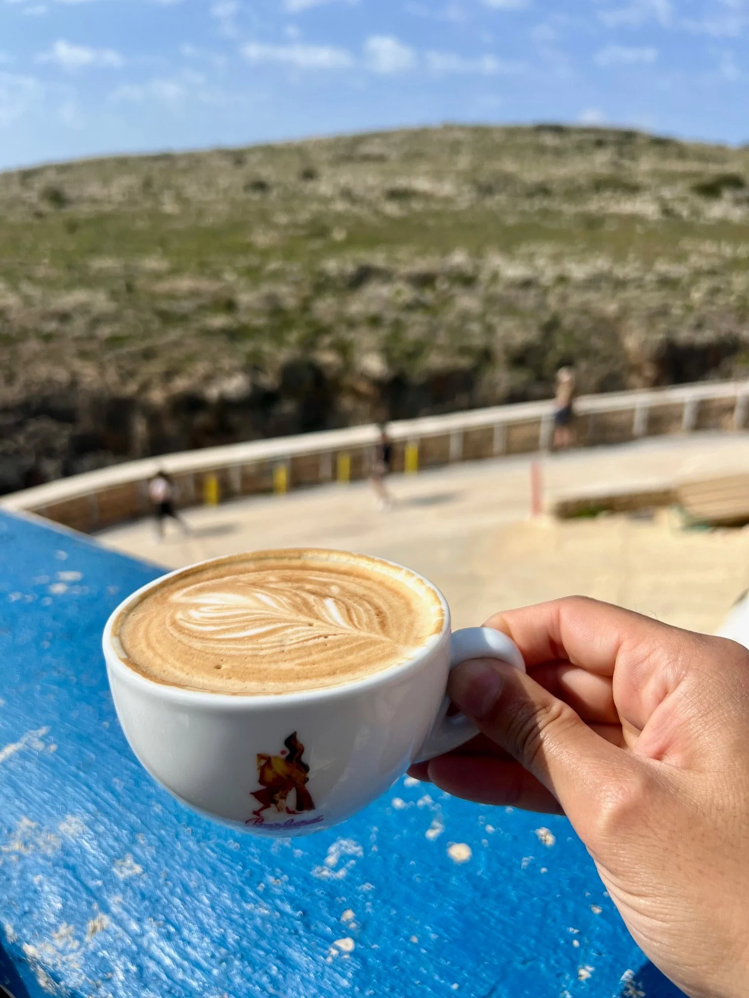 Holding a cappuccino cup with a view towards the cliffs at Wied iz-Zurrieq.