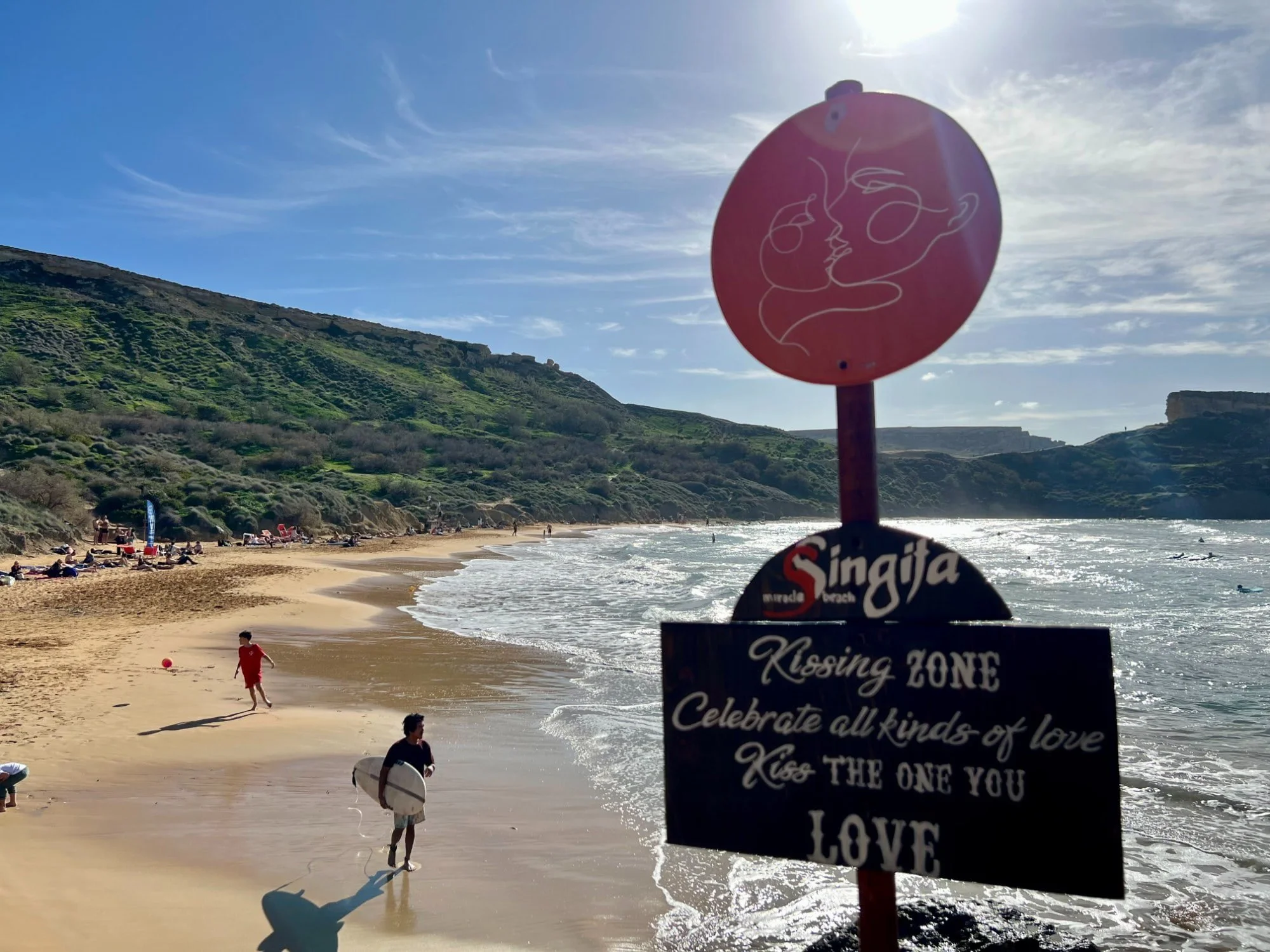 A surfer walking into the water past the red Singita Miracle Beach sign.