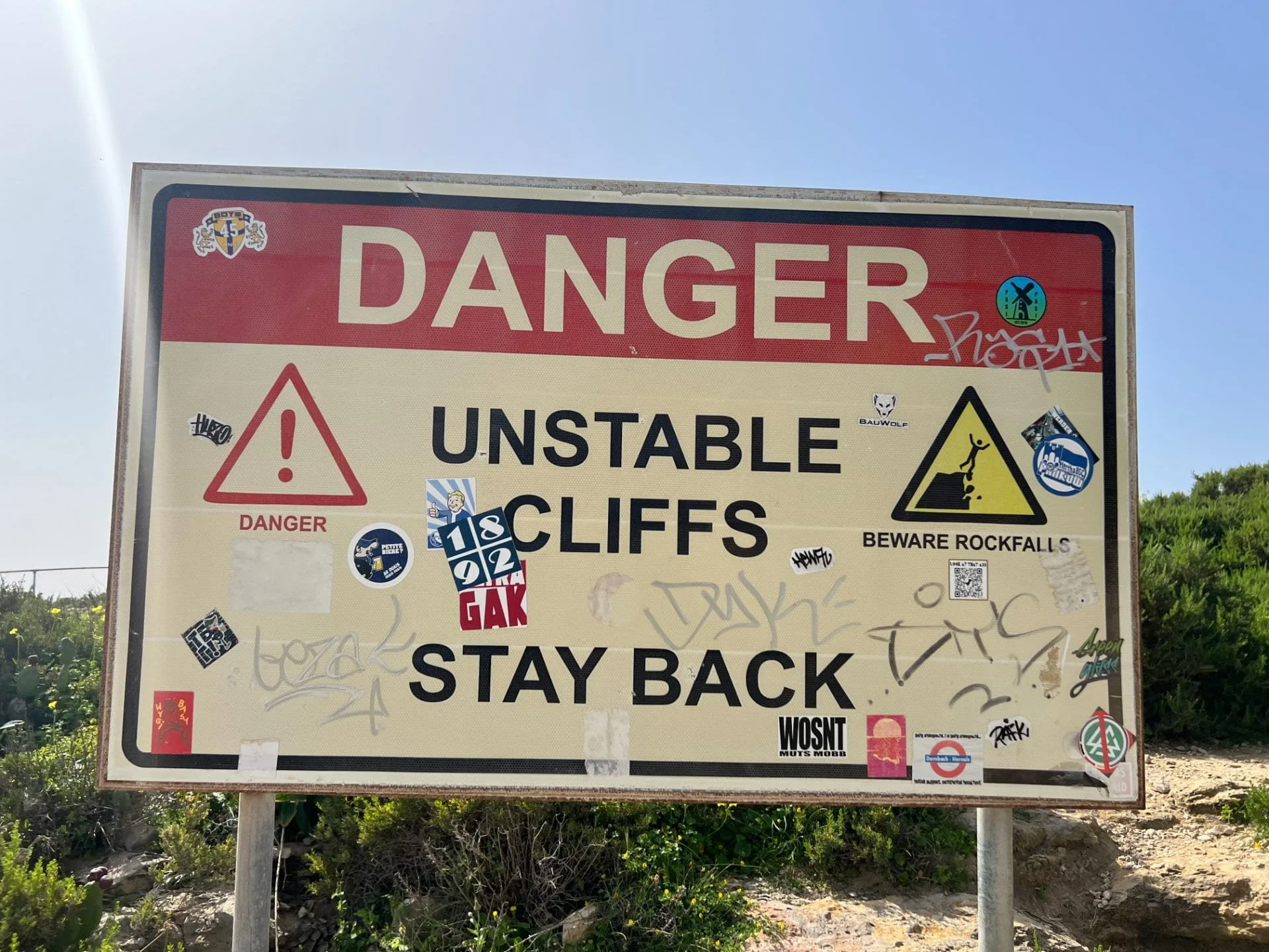 A warning sign near the coast reading Danger Unstable Cliffs Stay Back, highlighting erosion risks at the bay.