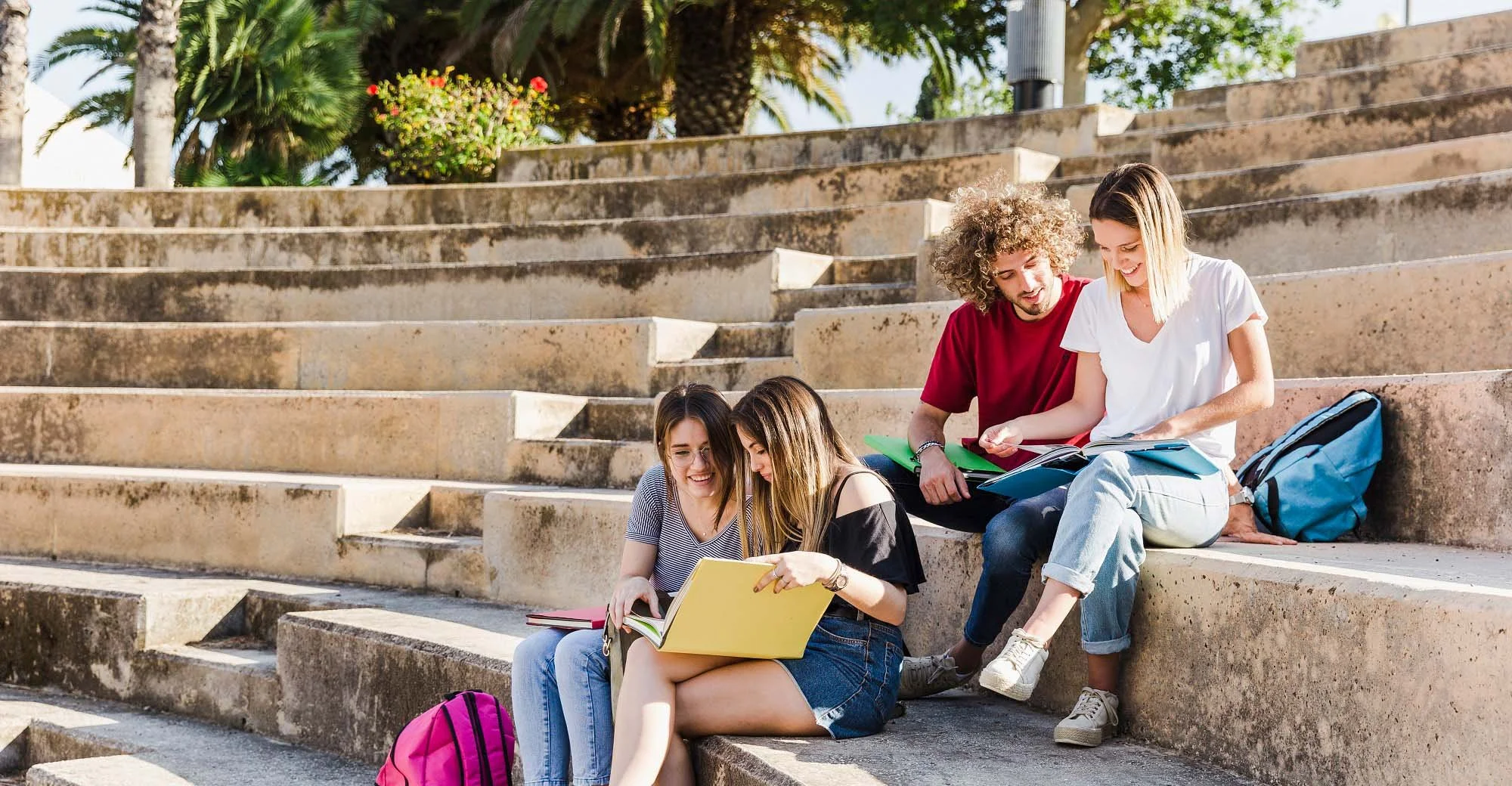 A diverse group of international students sitting on stairs outdoors in Malta, reading textbooks and studying together.