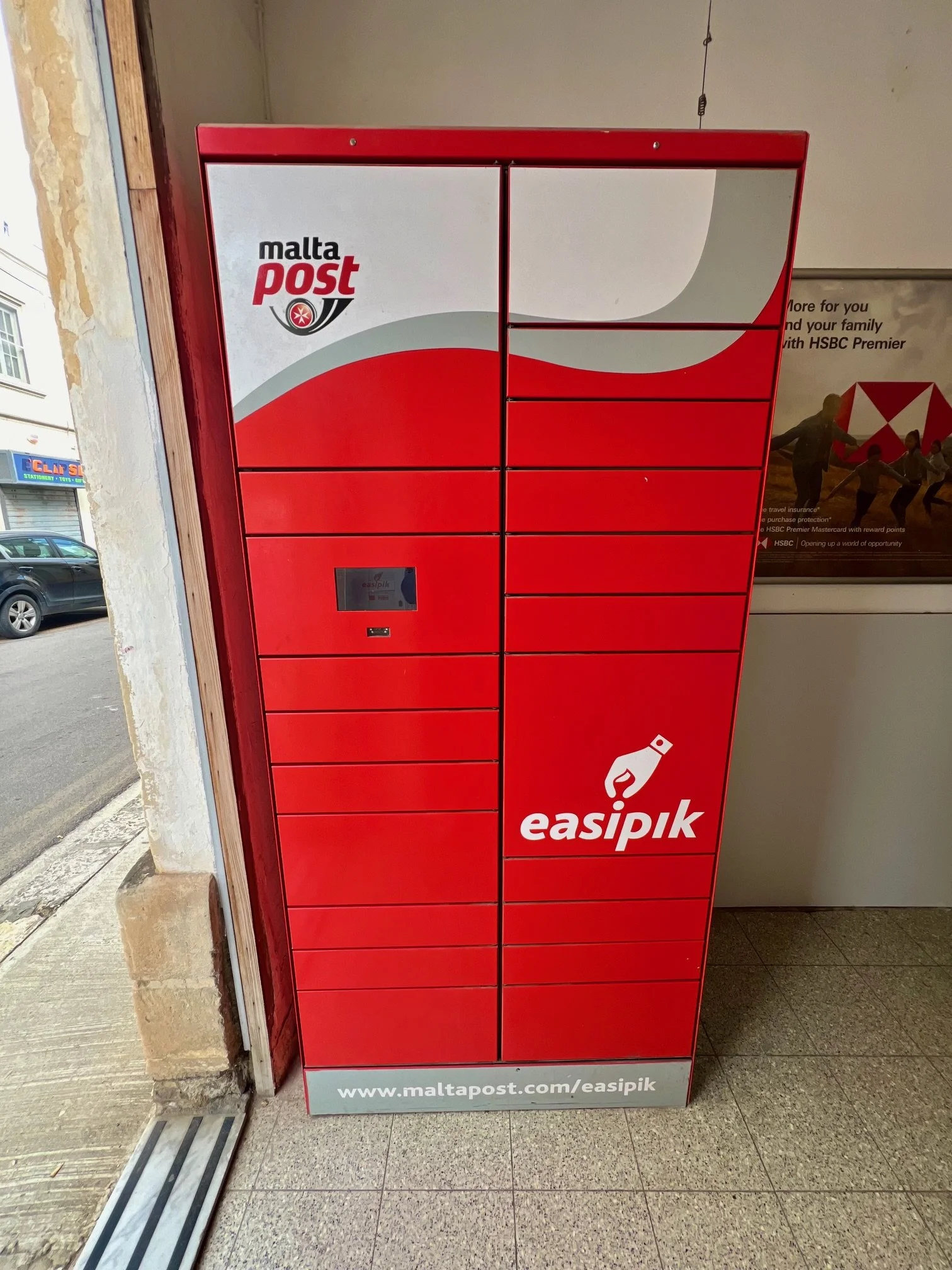 A red MaltaPost easipik parcel locker station located on a street in Malta.