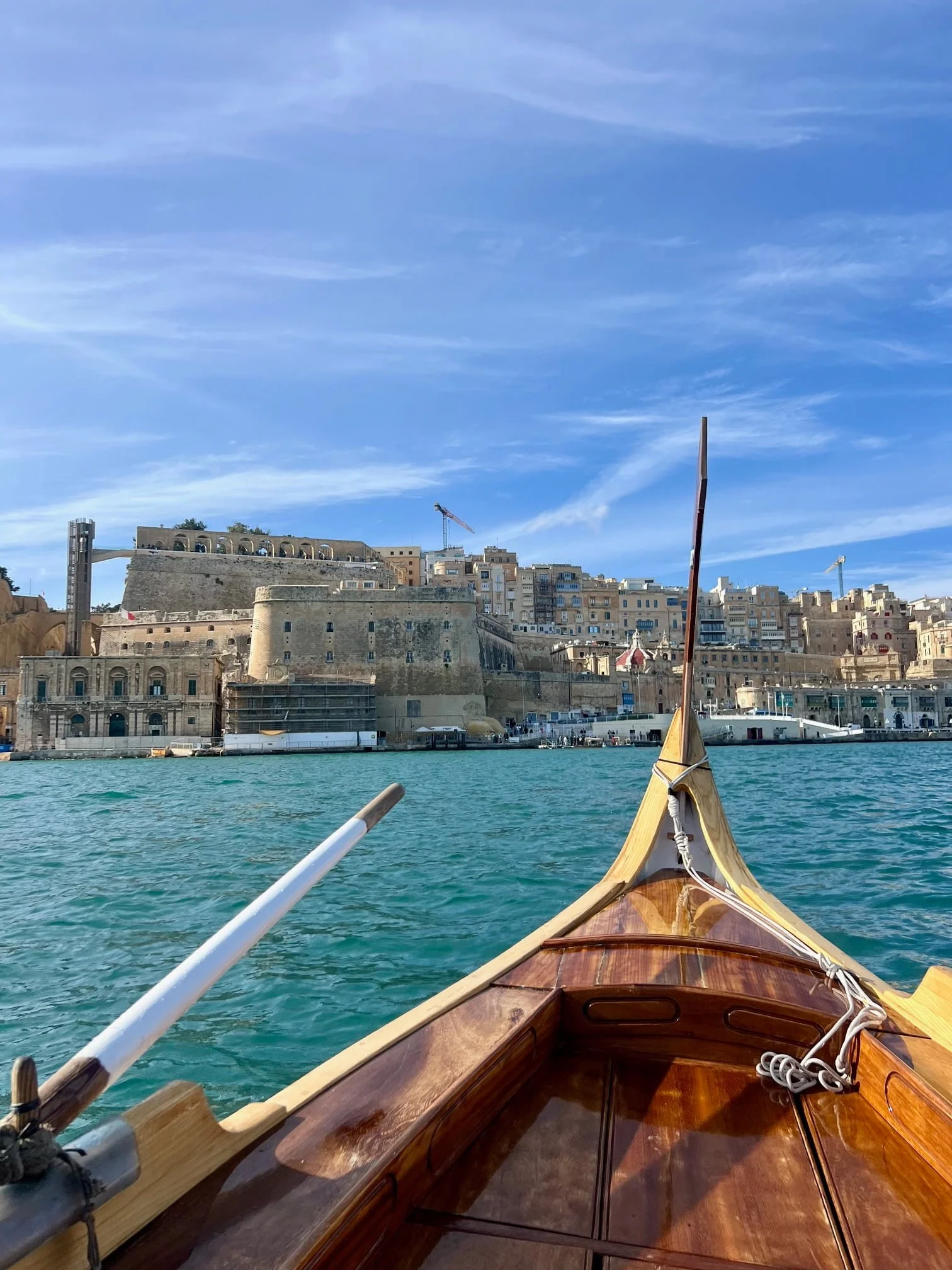 Traditional Maltese Dgħajsa boat crossing the Grand Harbour with Valletta in the background.