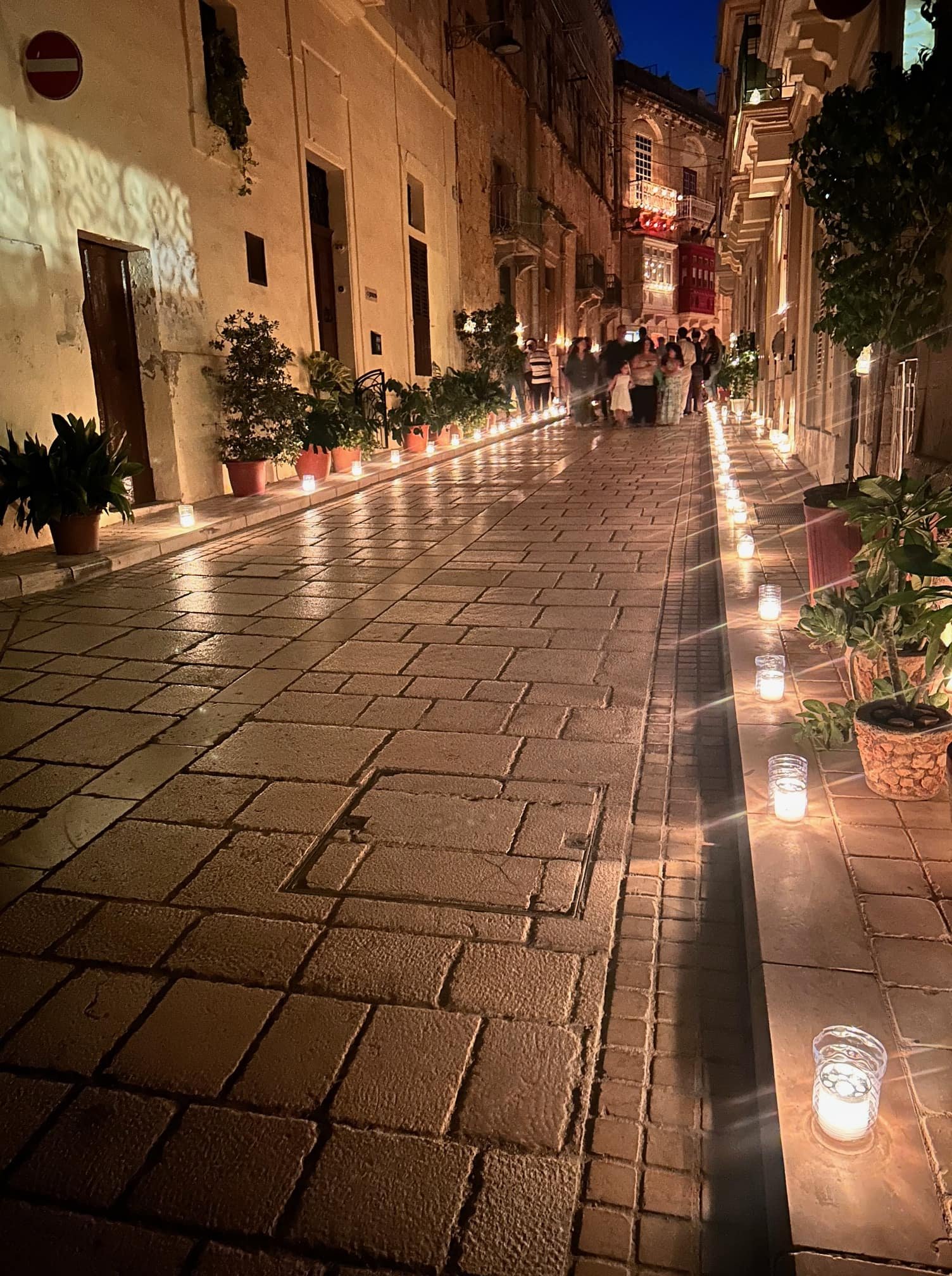 A narrow alley in Birgu illuminated by hundreds of candles lining the pavement at night.