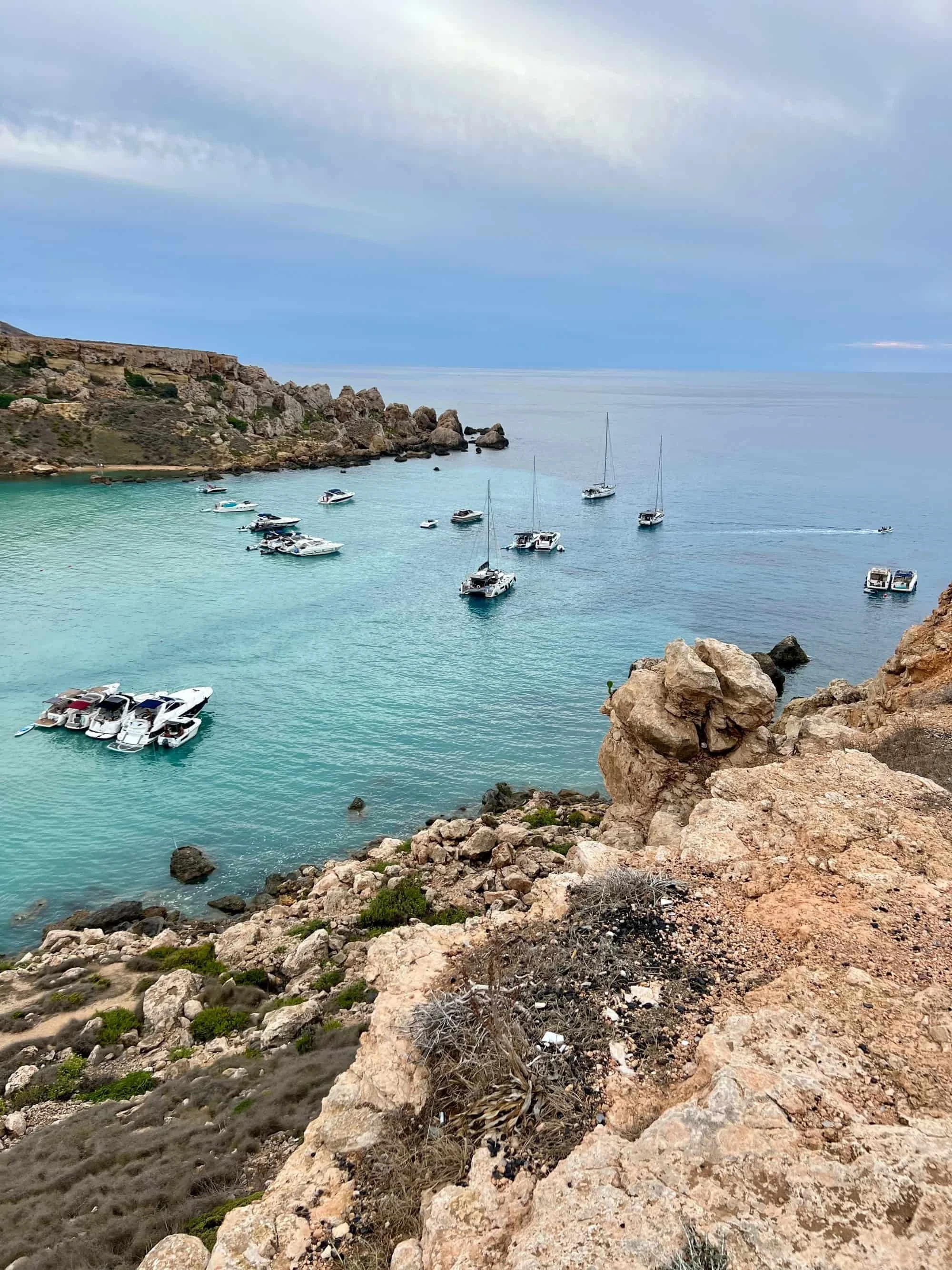 View from the cliffs looking down at boats anchored in the clear water near Gnejna and Riviera.