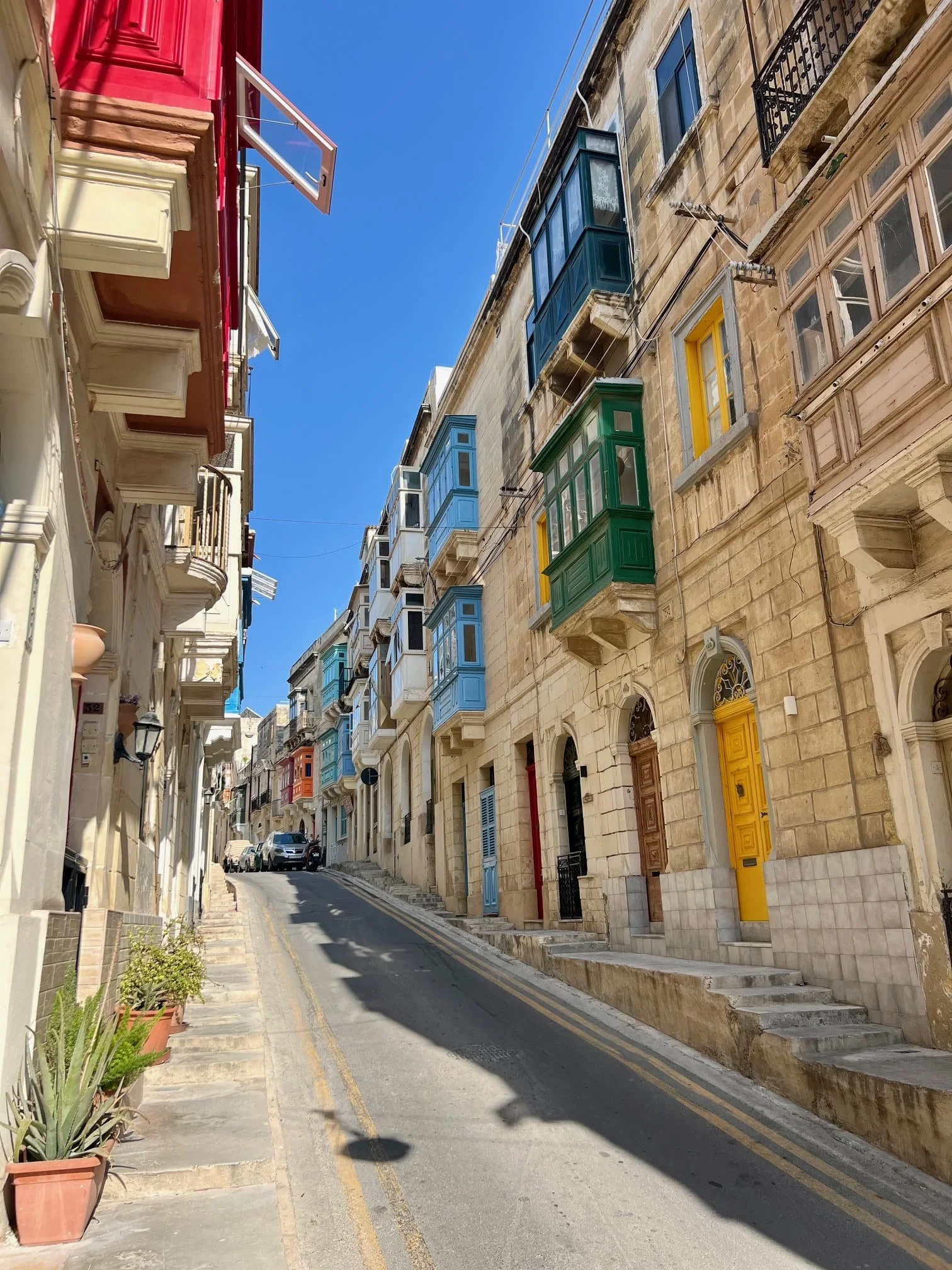 A steep uphill street in Cospicua lined with traditional townhouses and colorful wooden balconies.