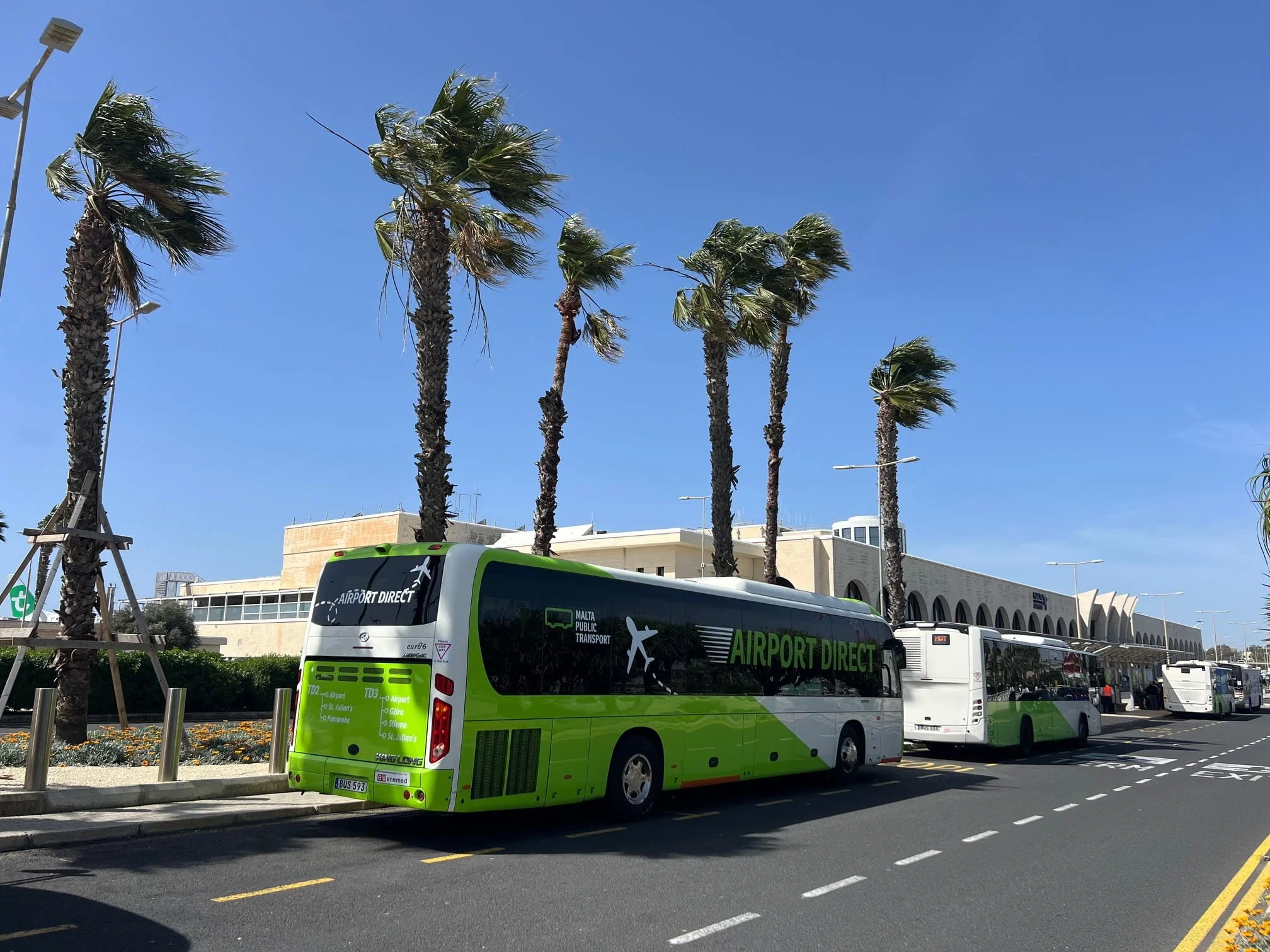 Green and white Malta Public Transport buses parked at the bus terminal outside Malta International Airport.