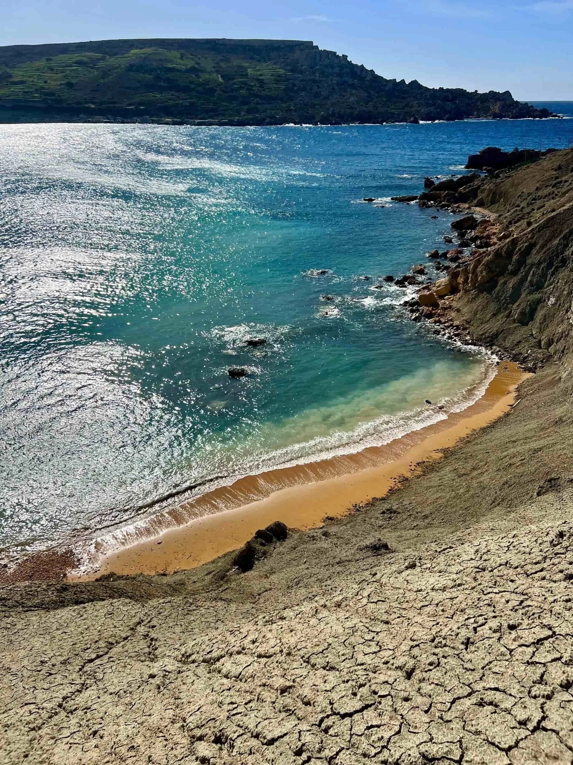 Looking down from the steep hiking path towards the sandy beach and turquoise water of Gnejna Bay.