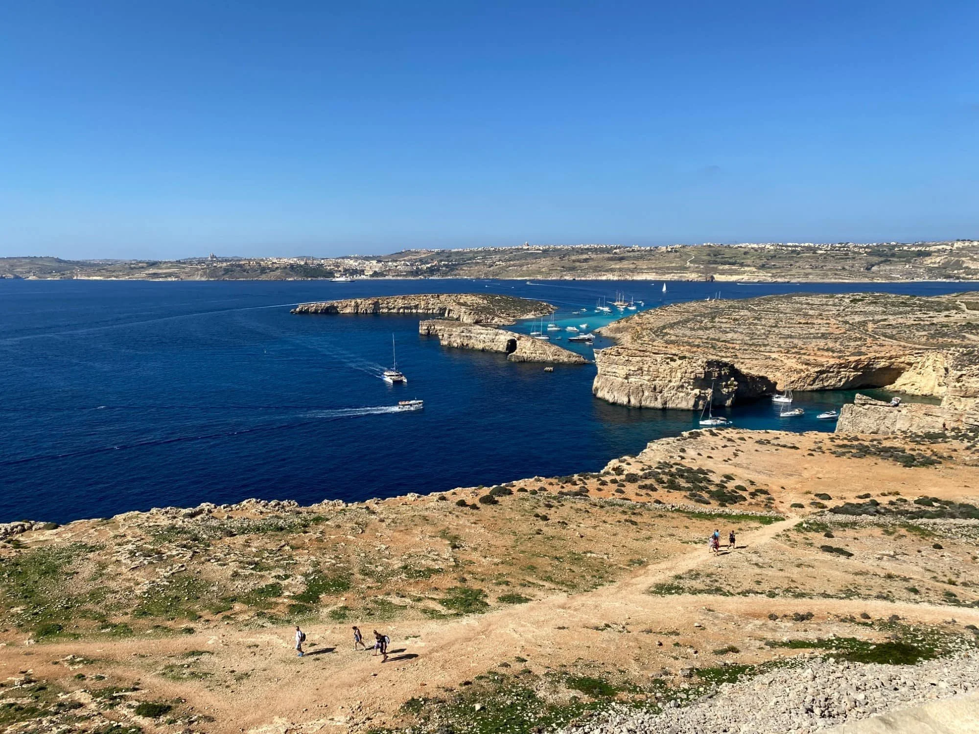 A dirt hiking path leading through the dry, rocky landscape of Comino Island with the sea in the background.