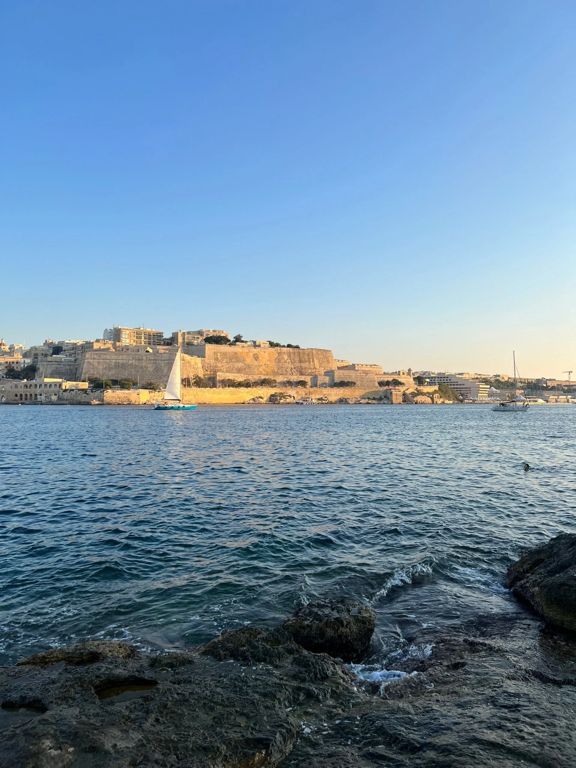 A swimmer enjoying the water at Stone Beach with the historic Valletta skyline in the background.
