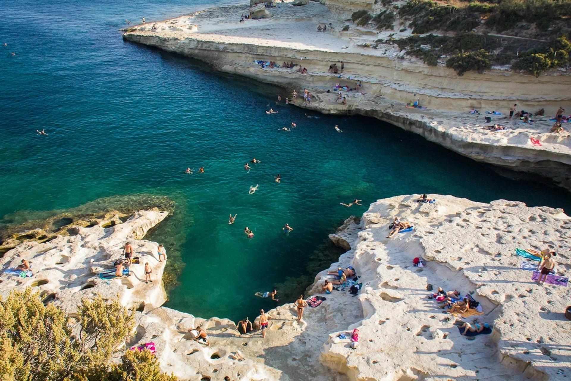 Swimmers and sunbathers enjoying the turquoise water and white limestone rocks at St. Peter's Pool natural swimming spot.