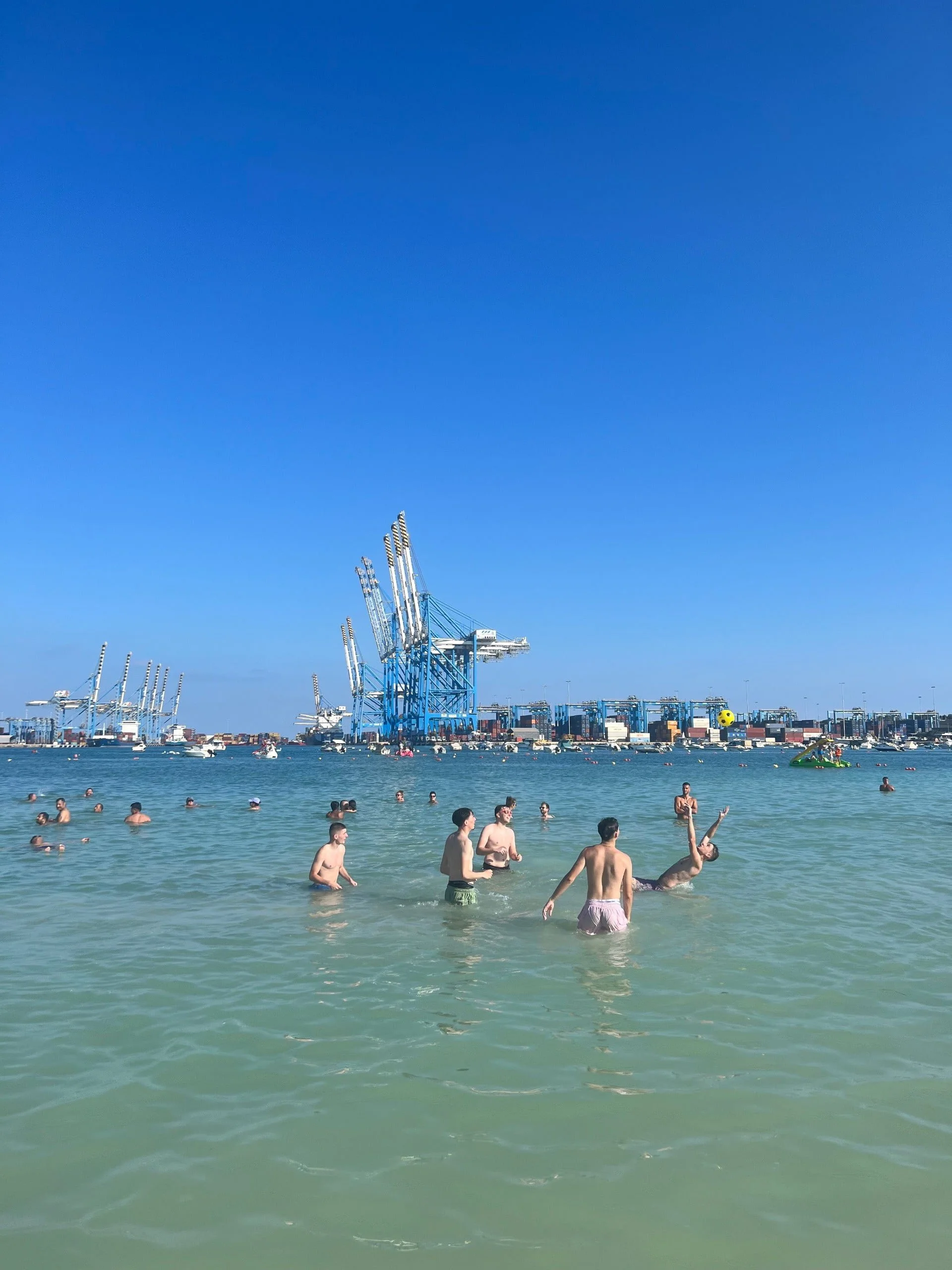 Swimmers enjoying the water at Pretty Bay with the large cranes of Malta Freeport in the background.