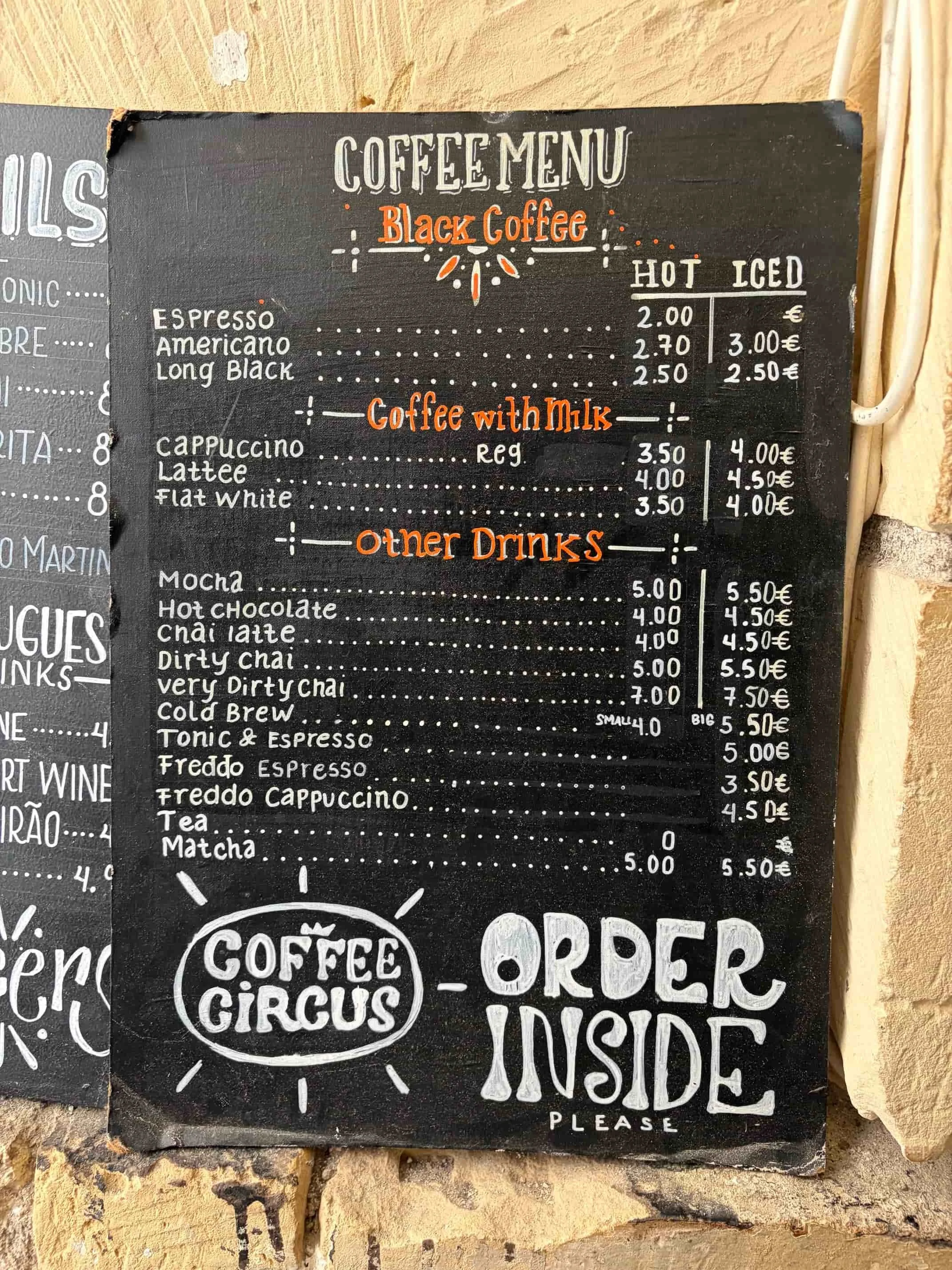 Handwritten chalkboard coffee menu hanging on the stone wall at Coffee Circus Lisboa, Valletta.