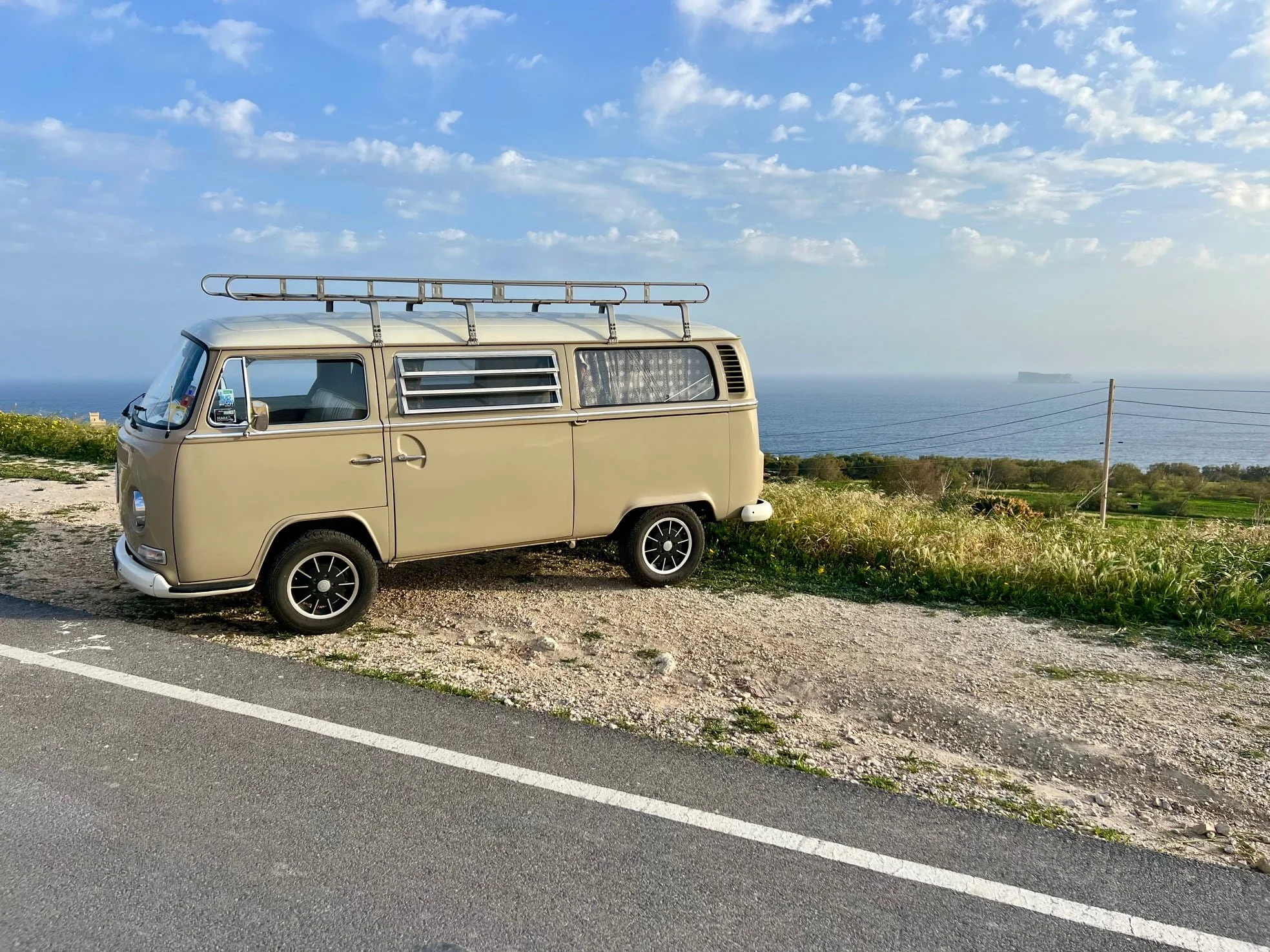 Beige vintage VW camper van parked on the side of the street overlooking the Maltese coast.