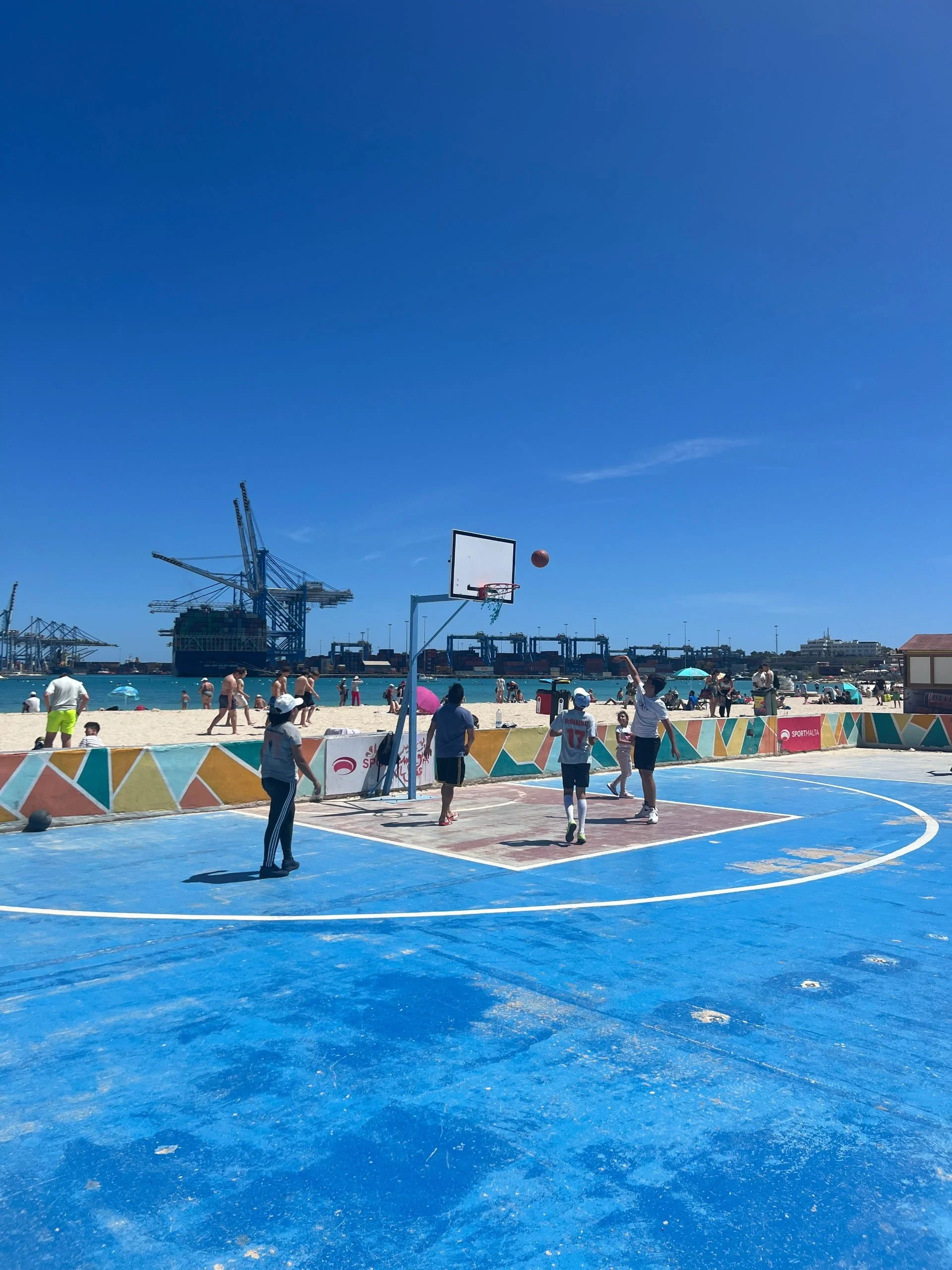 People playing basketball on the famous blue court right next to the sand at Pretty Bay.