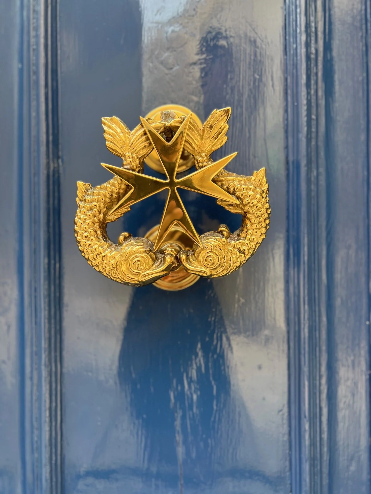 A detail shot of a traditional golden brass door knocker in the shape of a fish on a blue door.