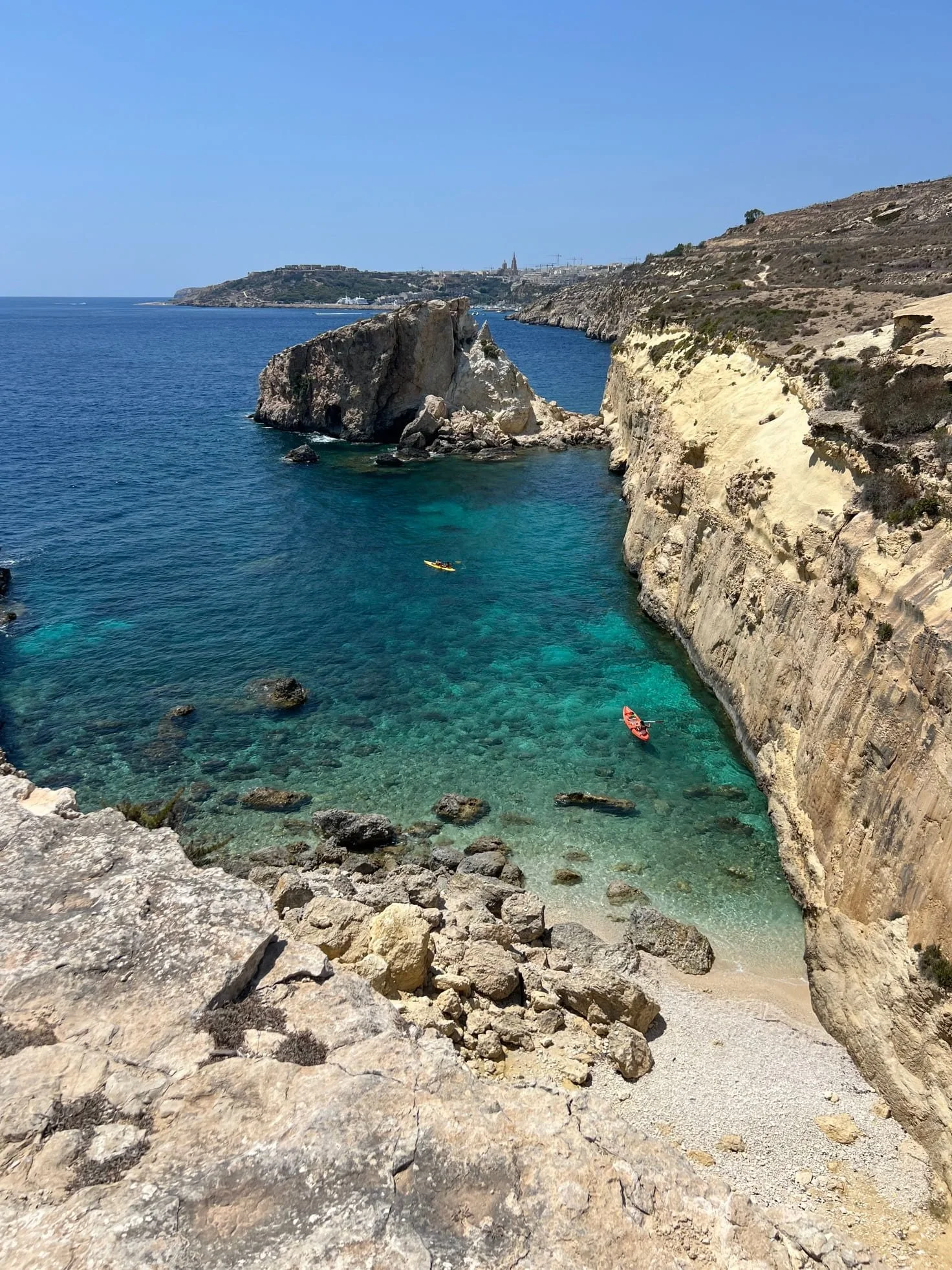 Two kayaks paddling through the deep blue water near the massive Barbaggan Rocks cliffs.