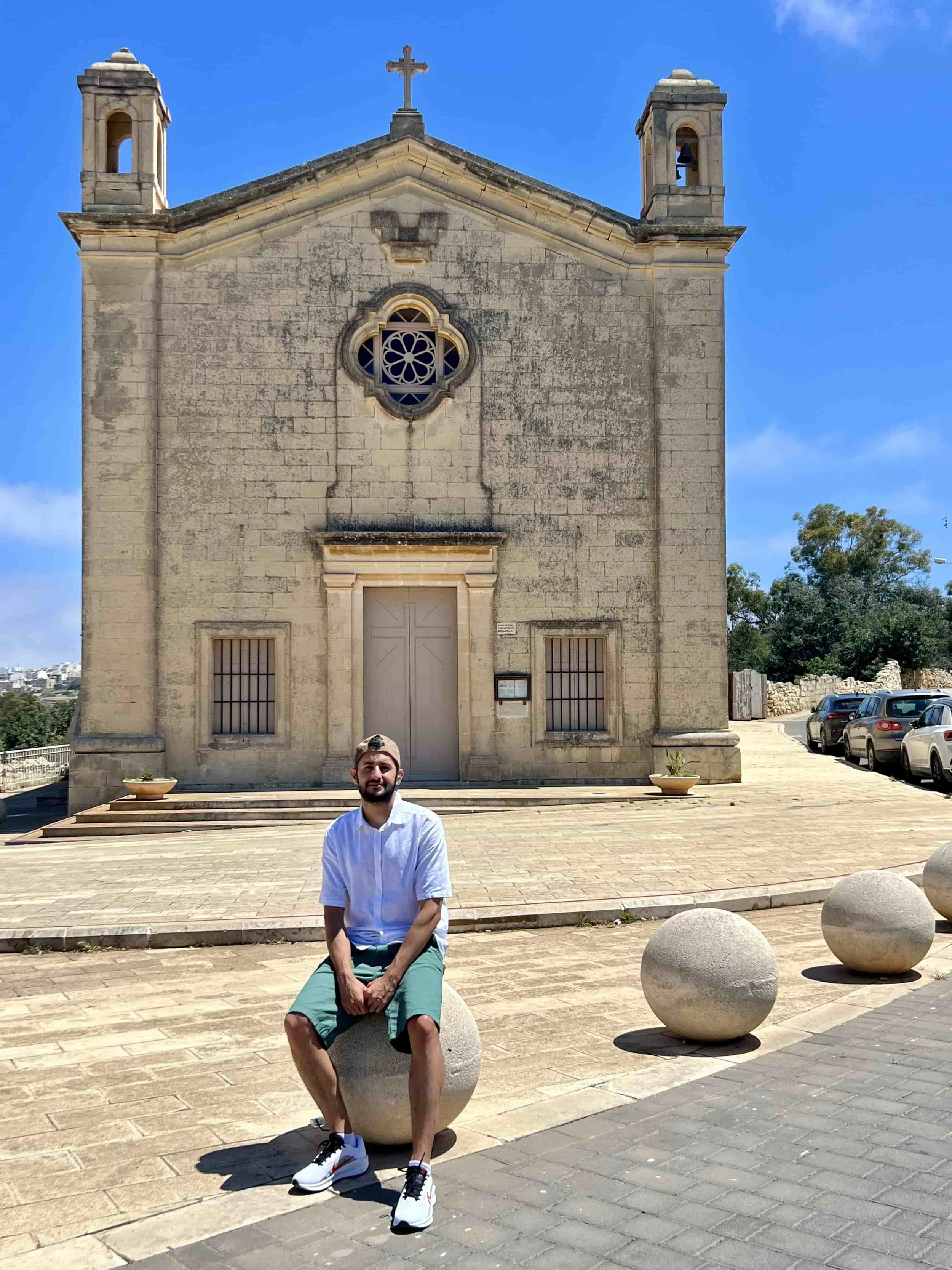 Bjorn, founder of ExplorinMalta, sitting on a round stone in front of the historic St. Matthew's Chapel in Qrendi.