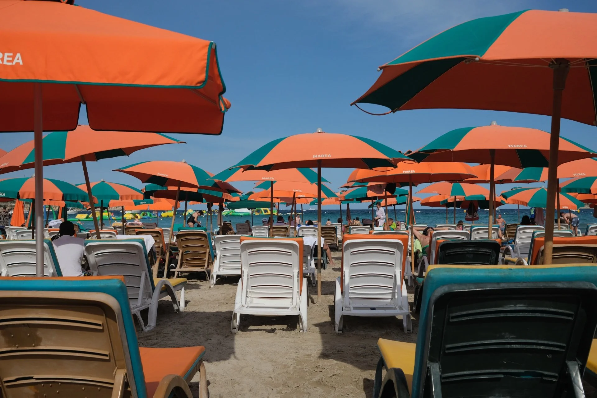 Orange and green sun umbrellas set up for rent on the sand at Mellieha Bay.