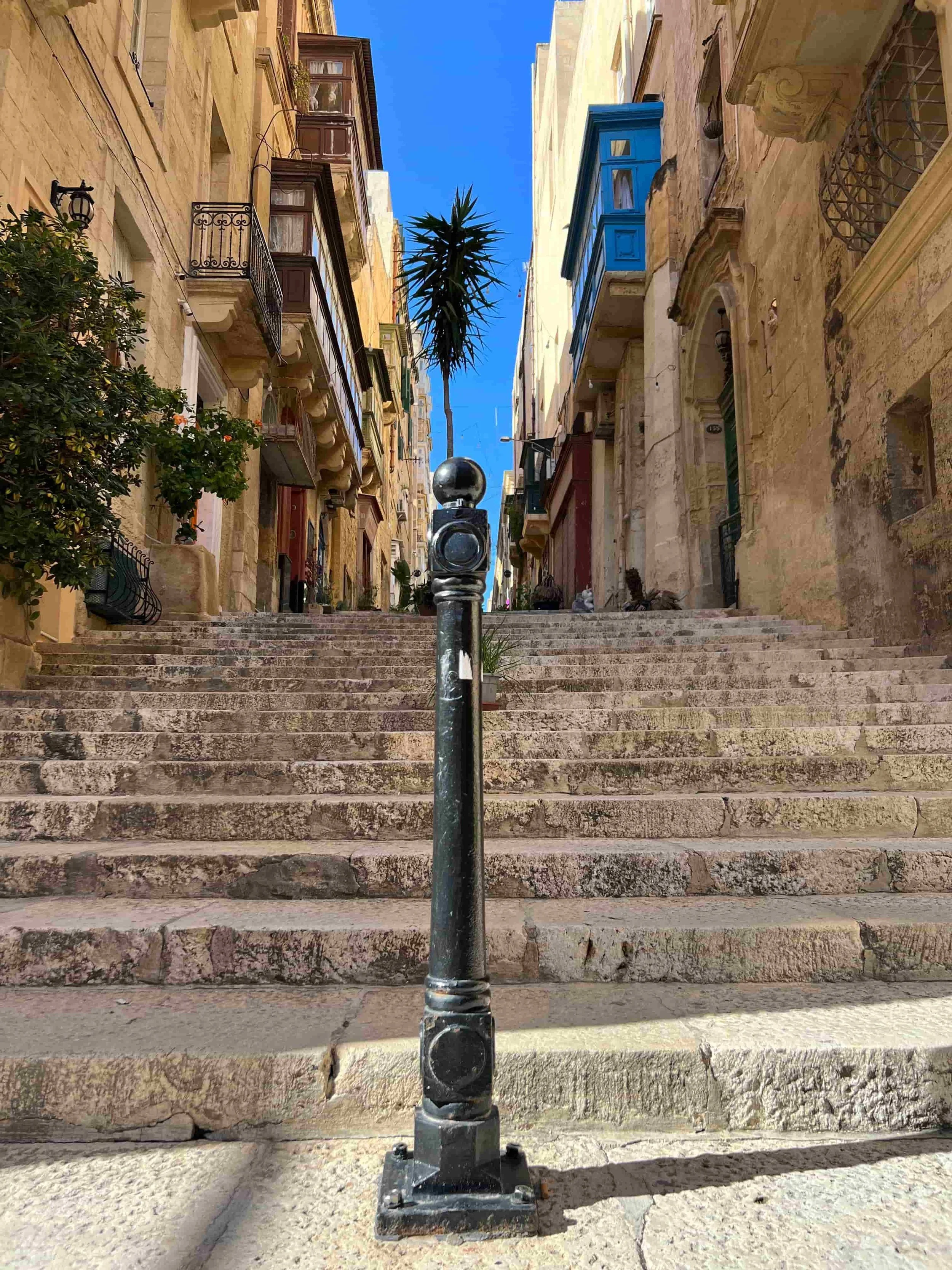 Steep limestone stairs in Old Theatre Street, Valletta, with a traditional iron bollard in the foreground.