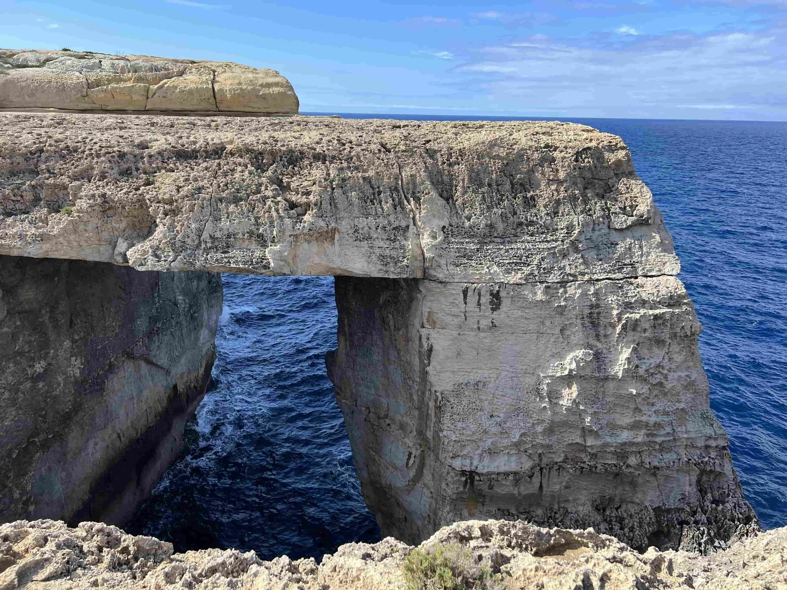 The rectangular natural rock arch of Wied il-Mielaħ stretching into the blue sea.