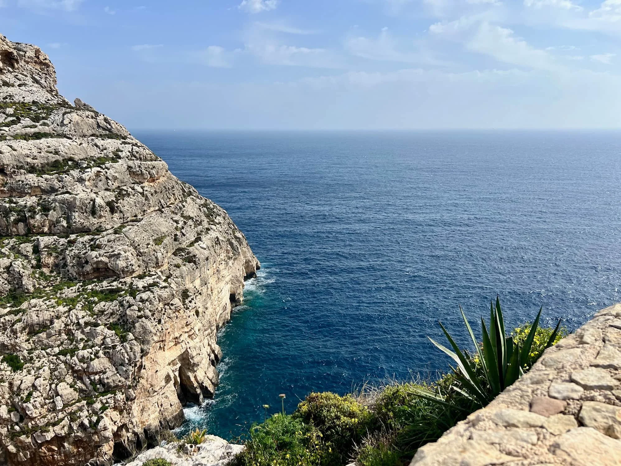 Steep cliffs and deep blue water at the Blue Grotto viewpoint in Malta.