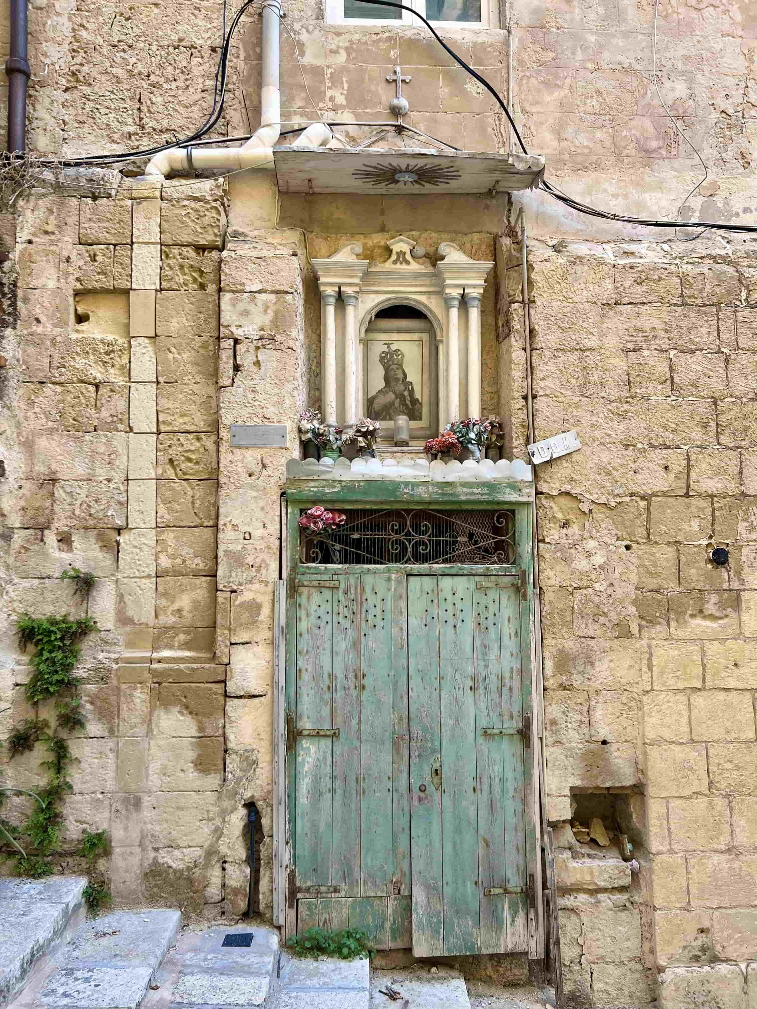 A small religious shrine of the Virgin Mary integrated into a limestone wall in Old Theatre Street, decorated with flowers.