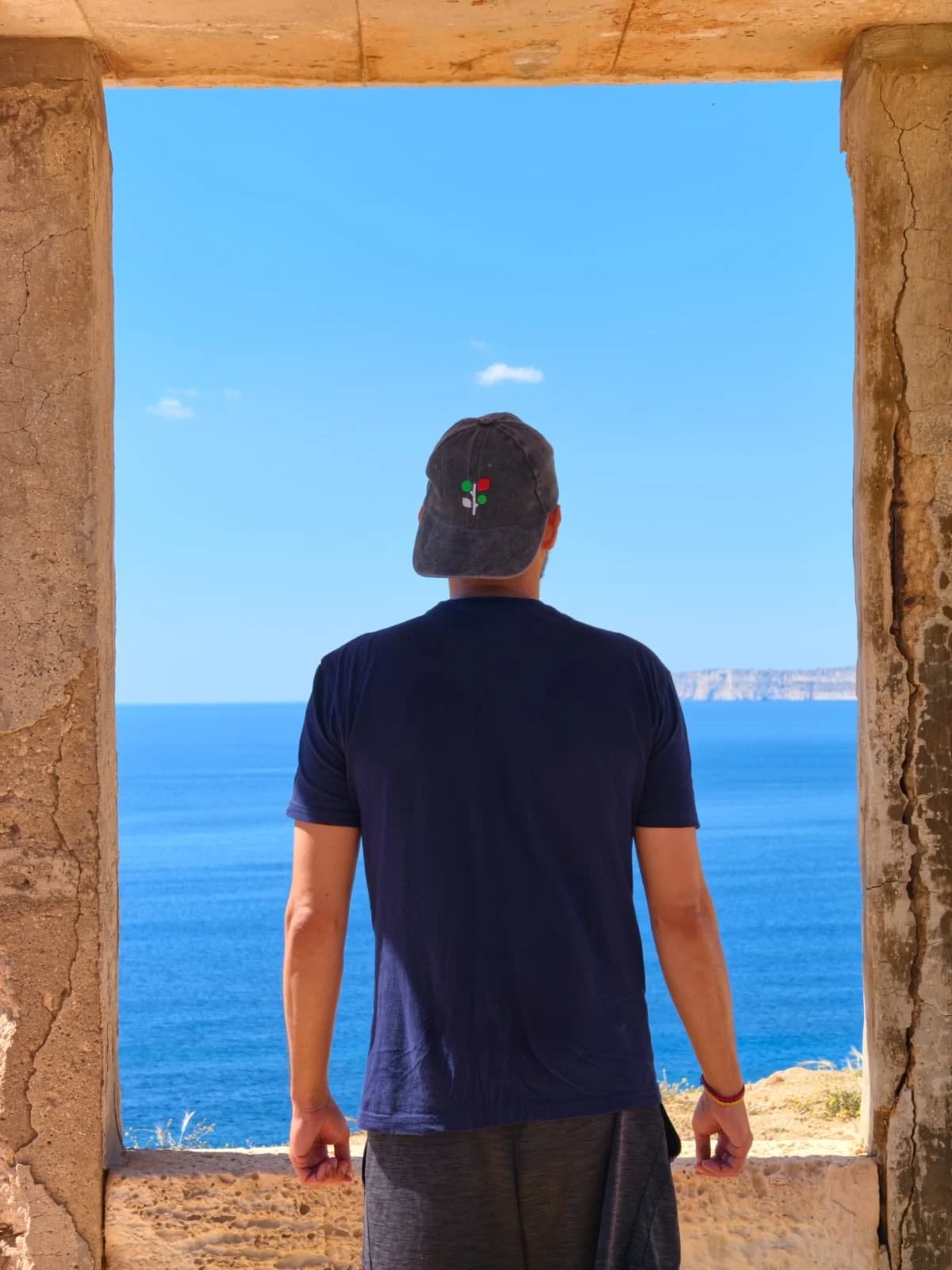 A person standing below a limestone structure looking out at the sea in Il-Majjistral Park.