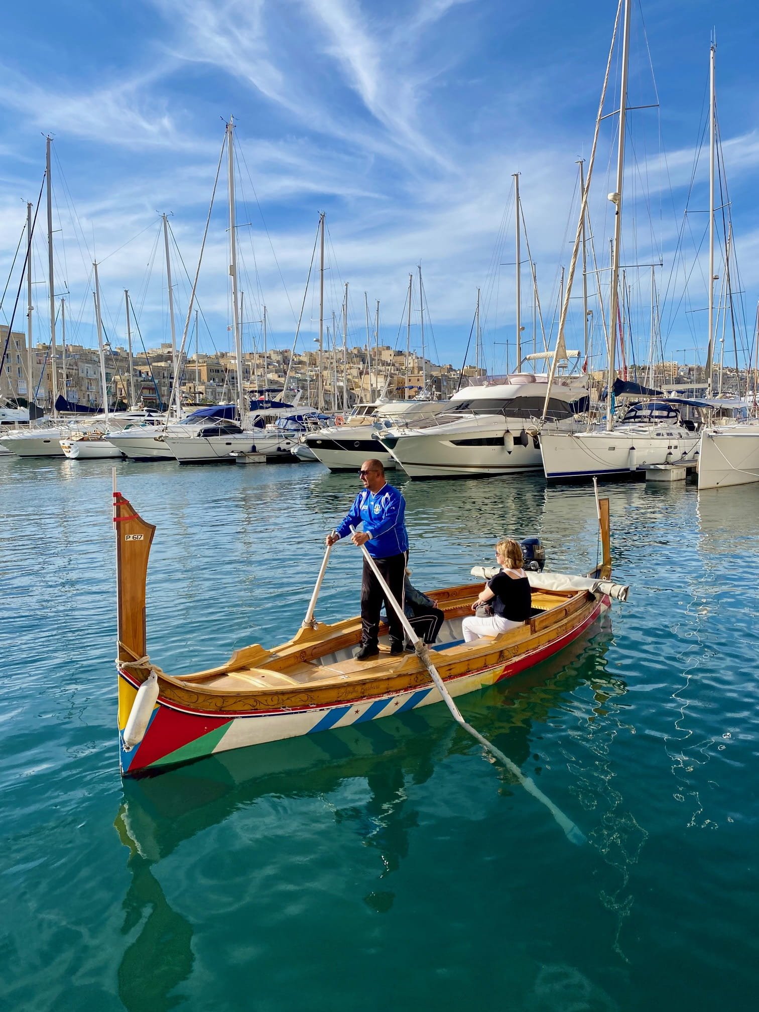 A boatman rowing a traditional Maltese Dghajsa boat across the Grand Harbour near Birgu.