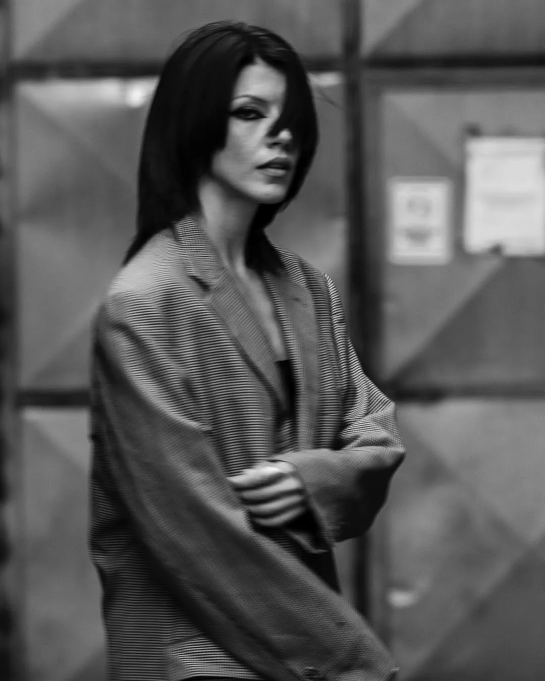 Black and white photo of a person in a plaid blazer, standing in front of a blurred industrial background.