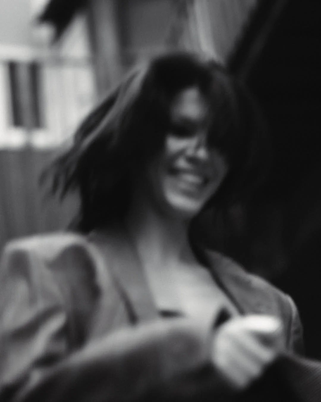 Black and white photo of a smiling person with a blurred motion, wearing a jacket.