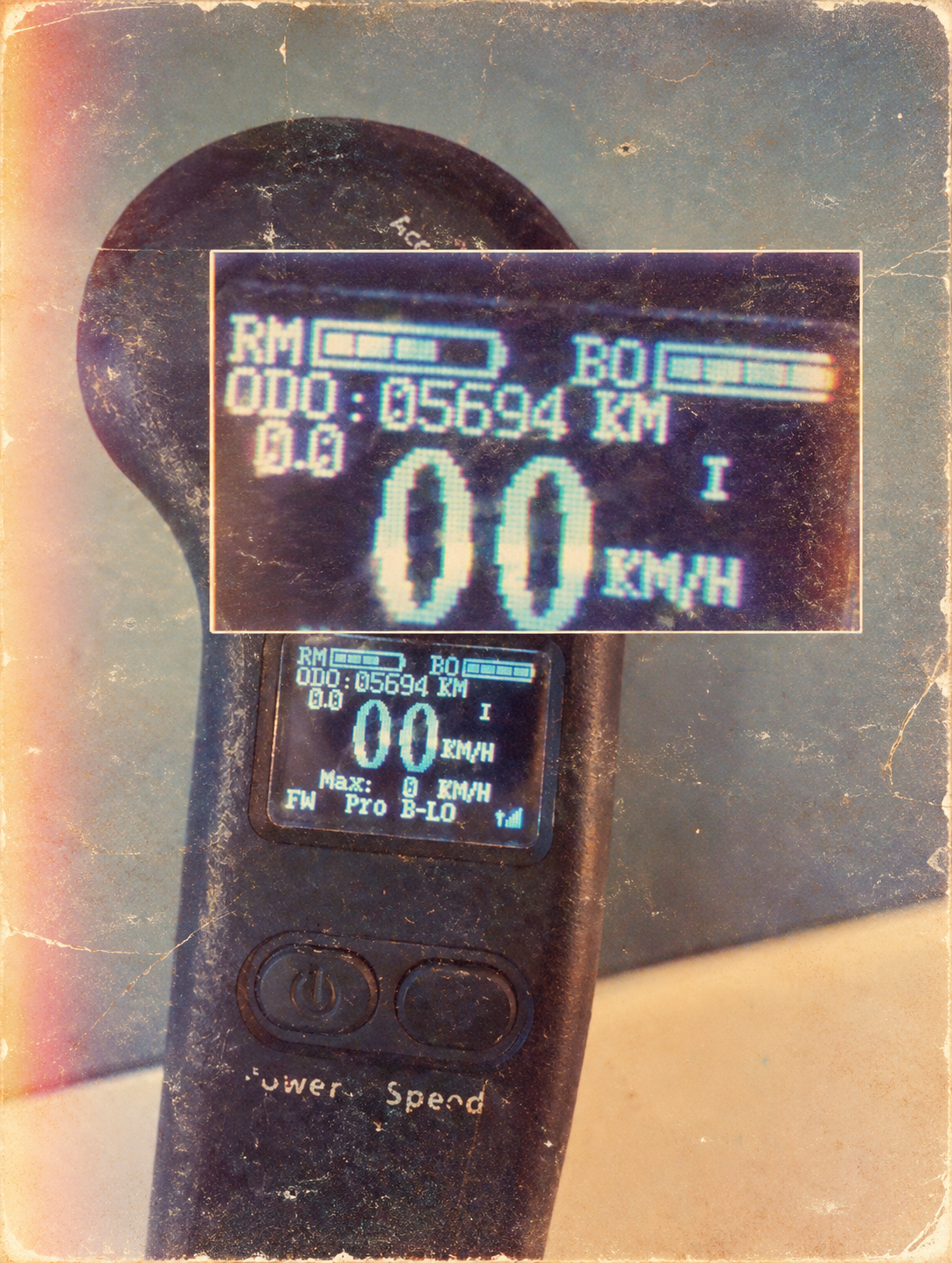 A digital display on an electric scooter showing 0.0 km/h speed, 5694 km distance traveled, and aBattery level, with another smaller screen showing similar information. The scooter has a power button and another button below it.