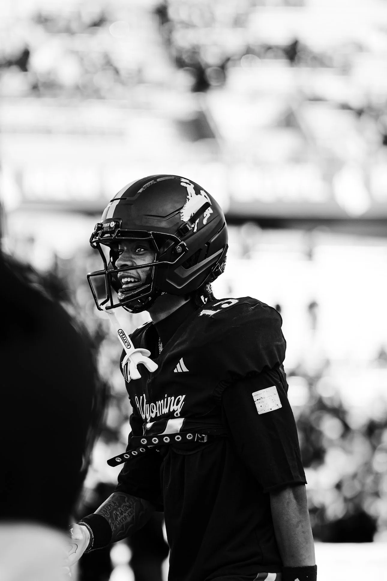 A woman football player wearing a helmet with a horse logo, smiling, and dressed in a Wyoming team uniform, standing on the field.