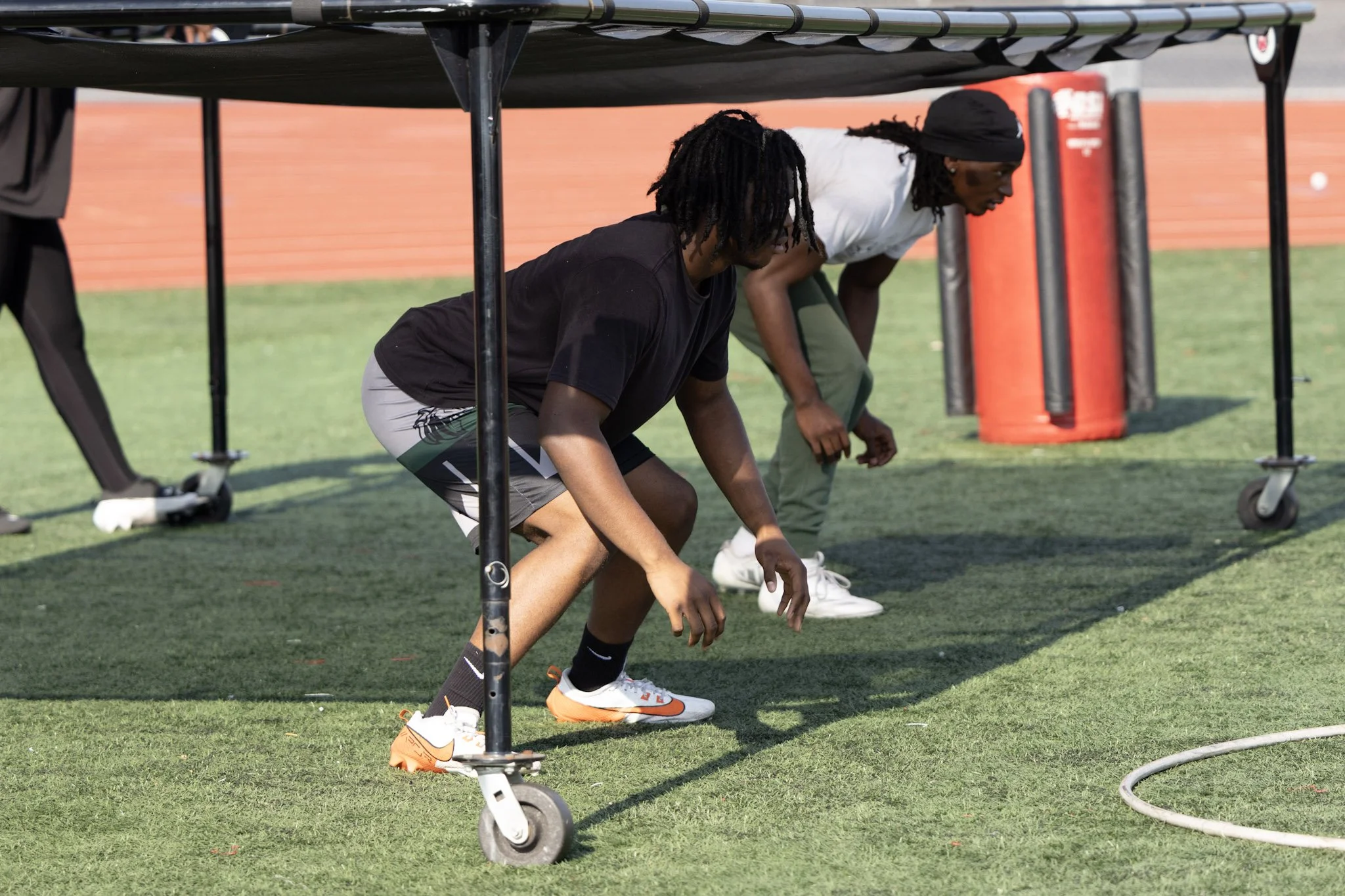 Two young men under a sports training table on a grassy field, preparing to do push-ups.