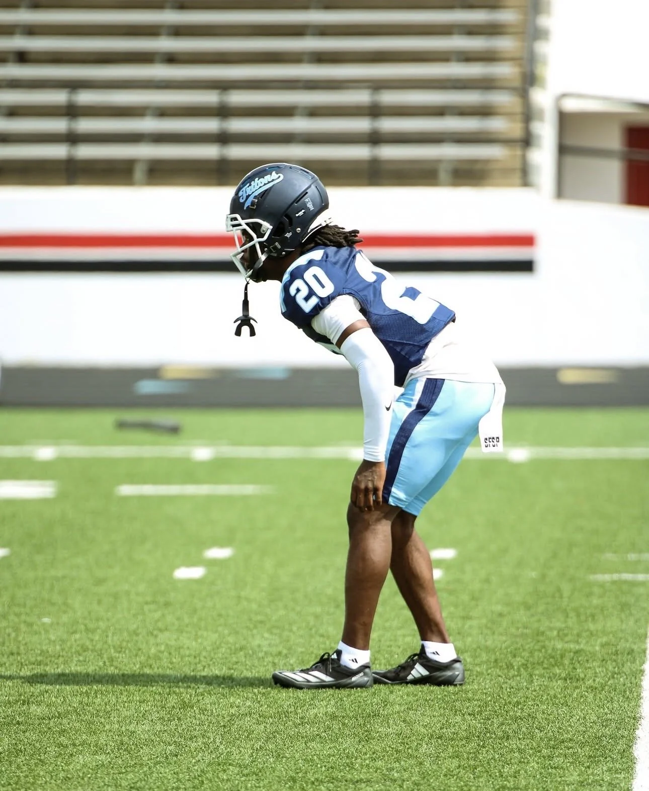 Football player wearing jersey number 20 preparing for a play on a green field.