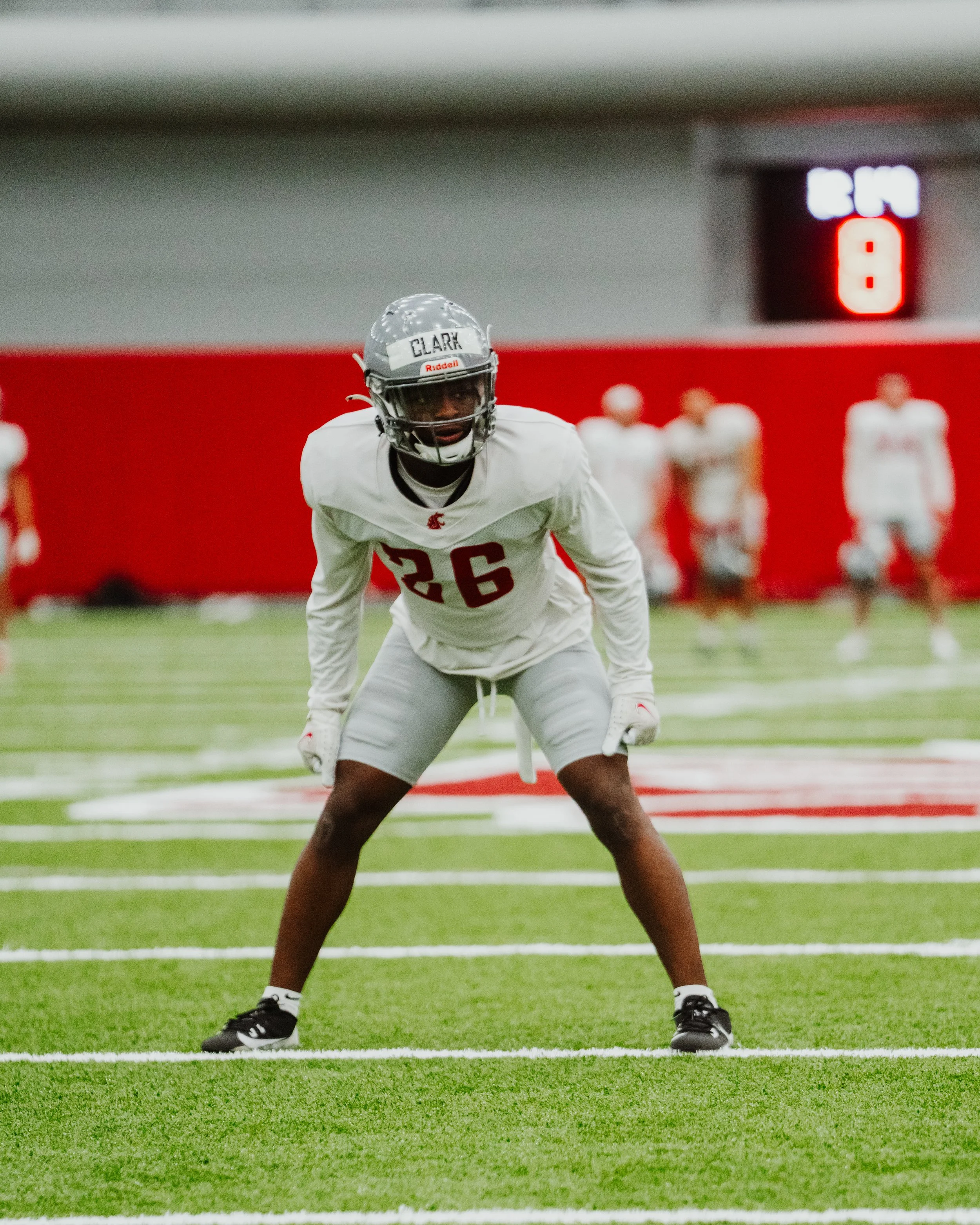 Football player wearing jersey number 26 in a ready stance on the field during practice or game, with scoreboard displaying 8 minutes remaining in the background.