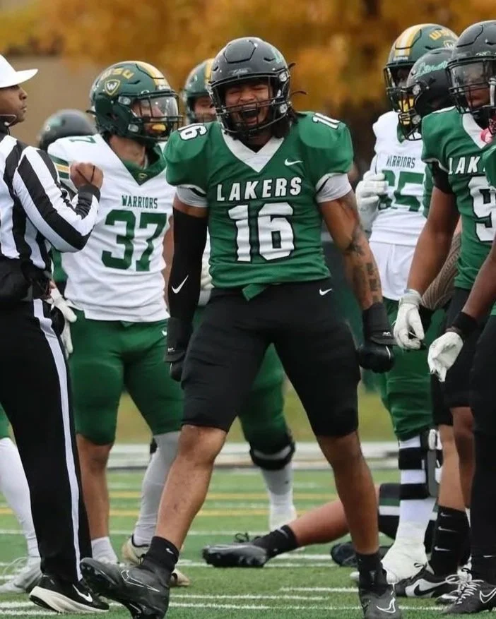 A football player in a green and white uniform with the number 16, standing on a field during a game with teammates and a referee nearby.