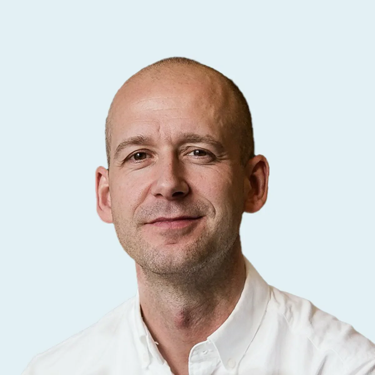 Portrait of a middle-aged man with a shaved head wearing a white collared shirt, smiling softly, against a light blue background.