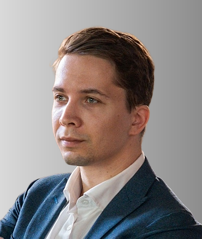 Portrait of a young man with short brown hair, wearing a white dress shirt and navy blazer, against a gray background.