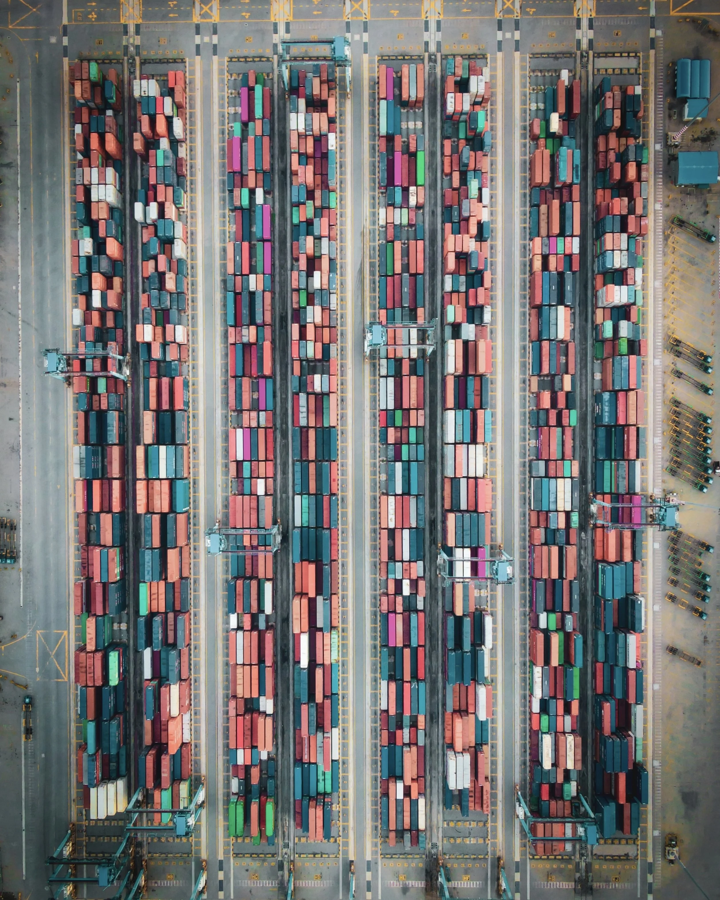 An aerial view of a large shipping container yard with rows of multicolored containers and cranes.