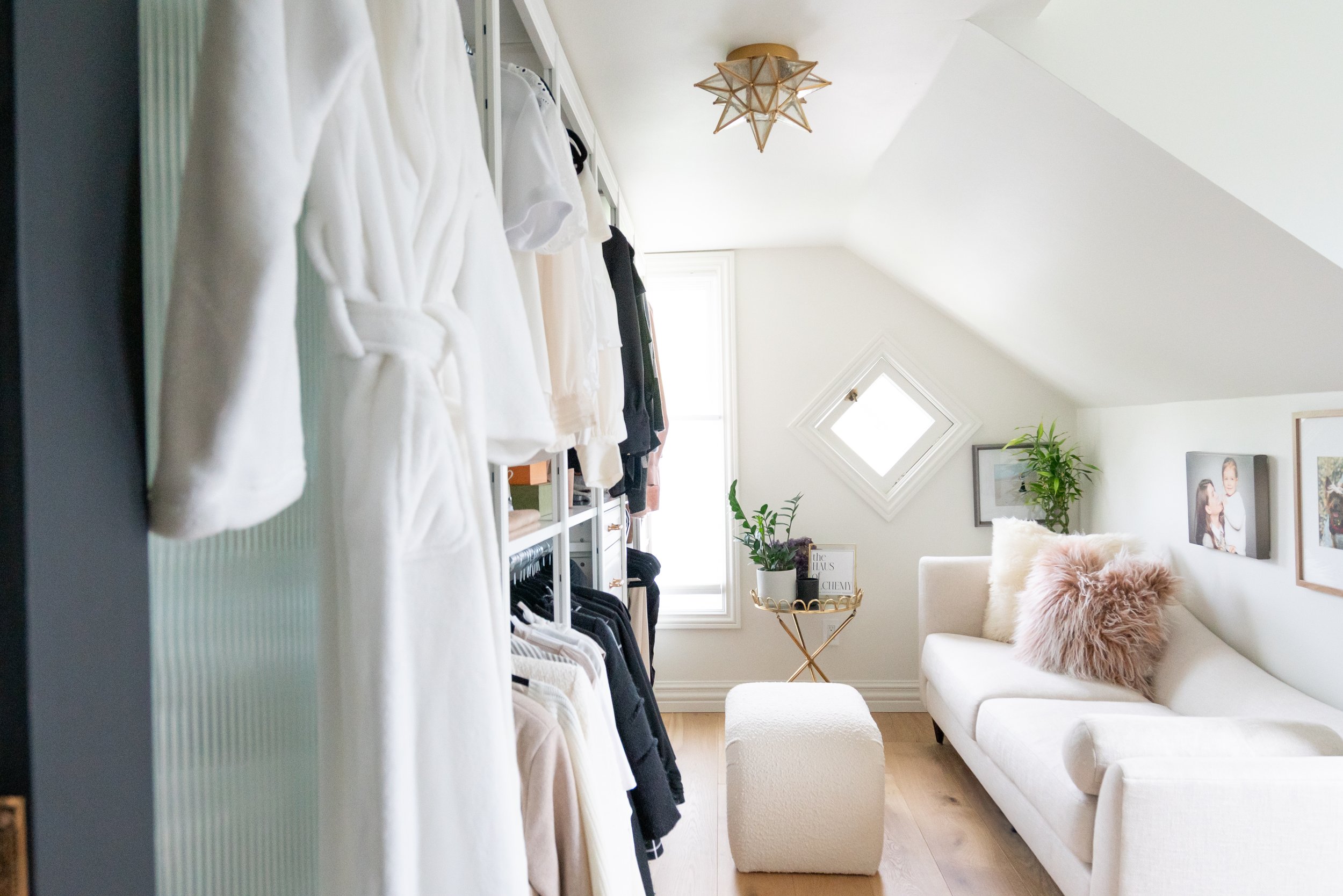 interior design of a light closet with a chaise lounge and ottoman, greenery and light wood floors with dark fluted glass doors