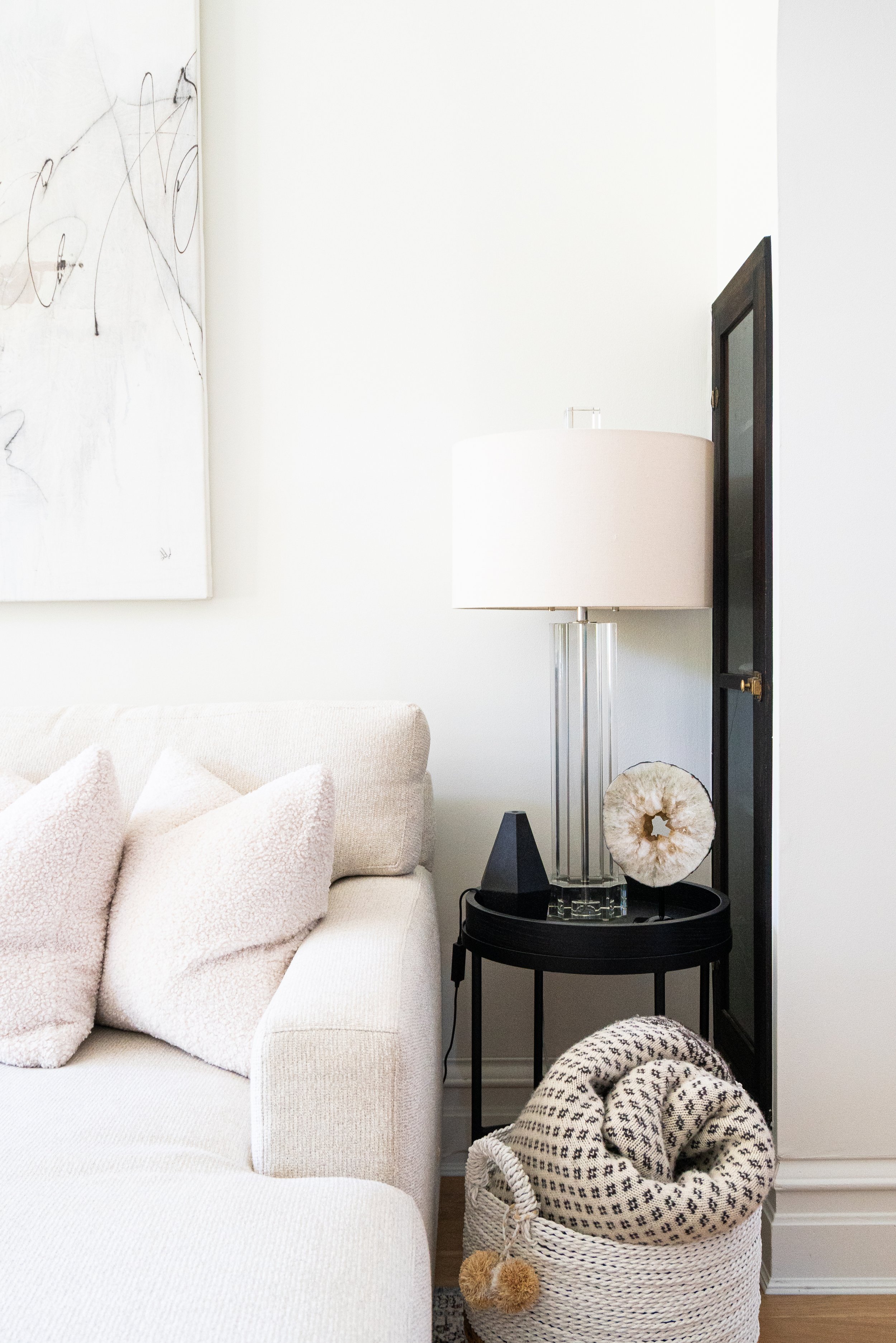 interior design of a light and airy living room with a white sofa, large piece of art, small end table with a lamp