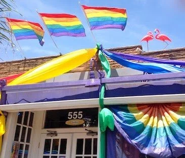 Rainbow flags and decorations with flamingo statues on a building.