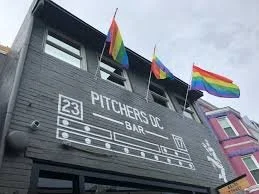 Building facade with rainbow pride flags and sign reading Pitchers Up Bar along with a sports field diagram.